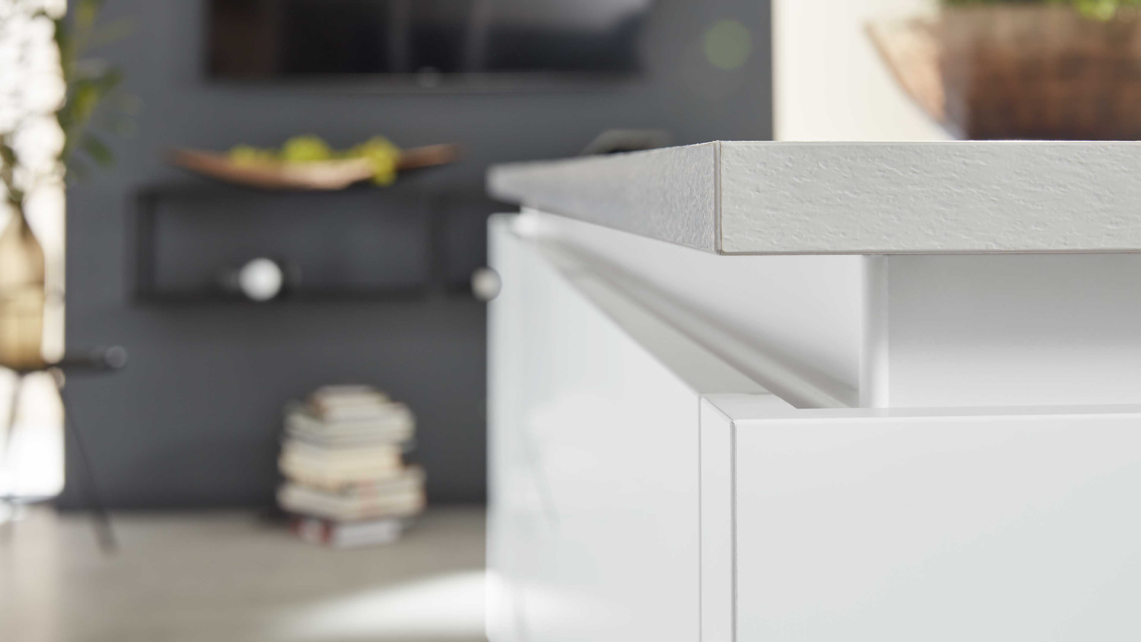 Nahaufnahme eines weißen Schubkastens mit integrierter Griffleiste und heller, strukturiert wirkender Aufsatzplatte.