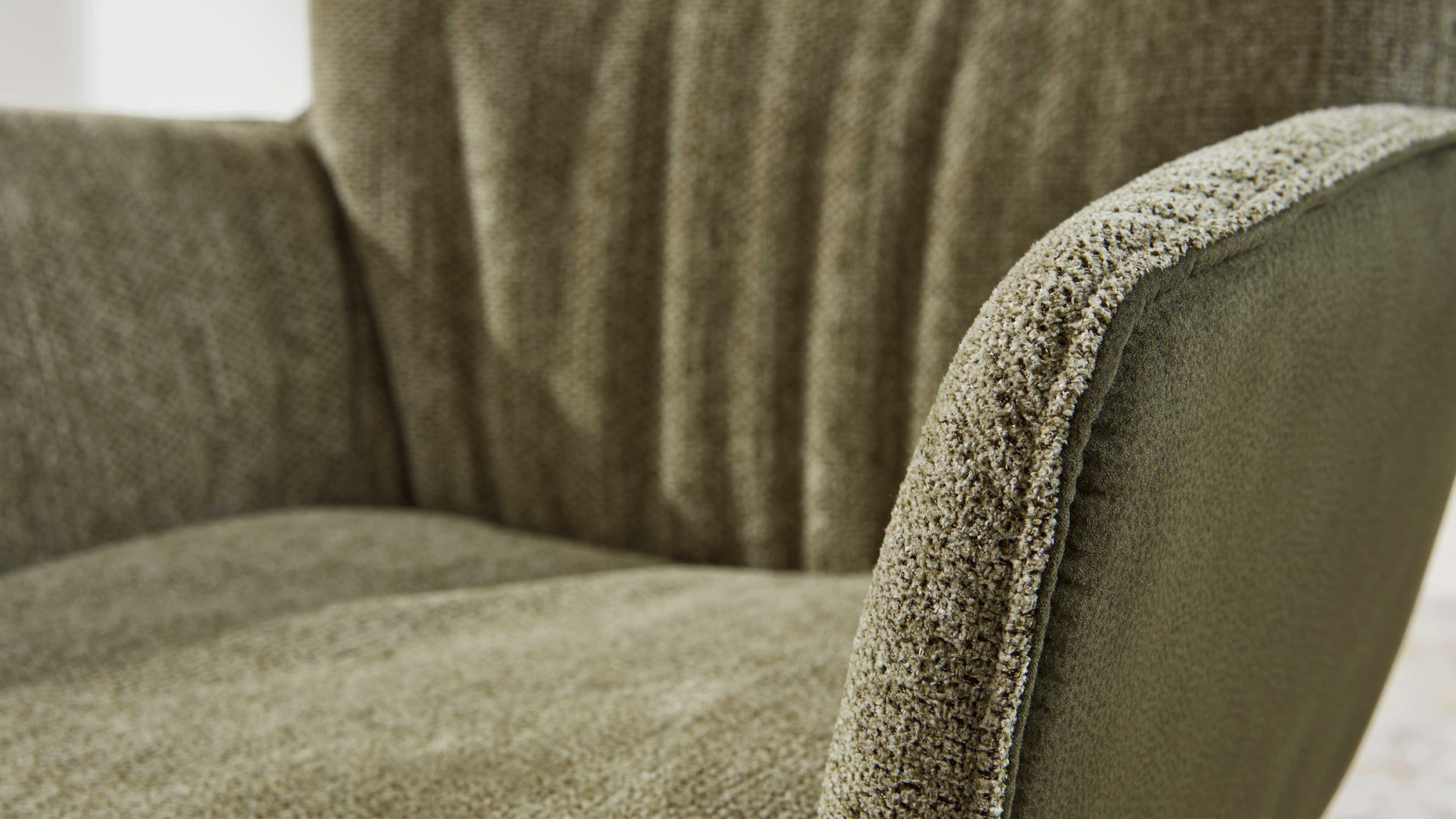 Nahaufnahme eines olivgrünen Polstersessels mit gerundetem Armlehnenbezug und strukturierter Stoffoberfläche.