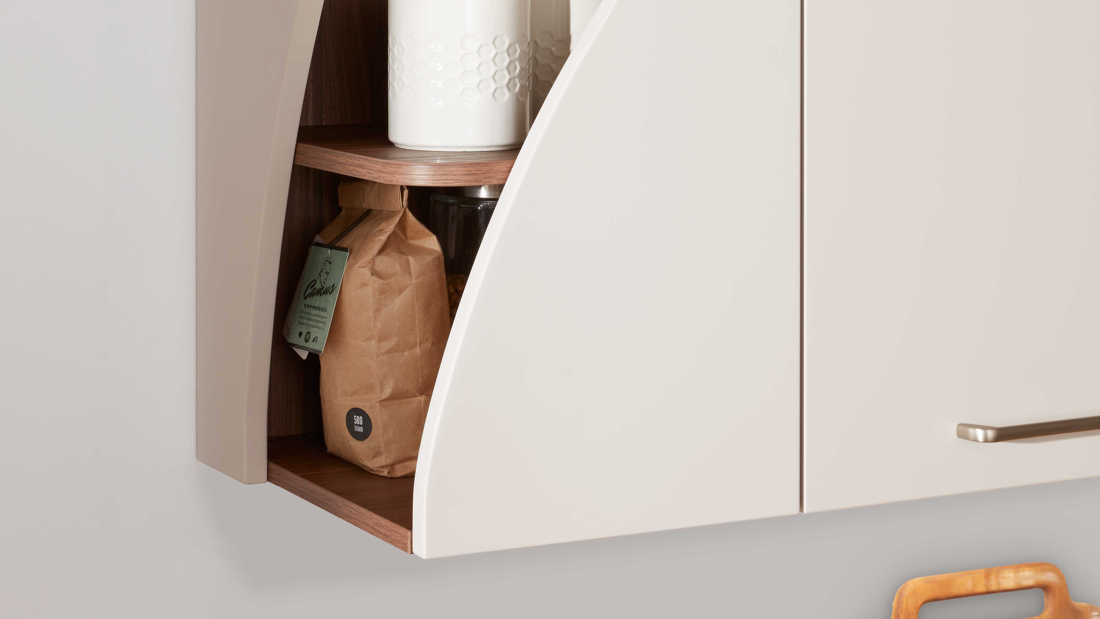 Wandhängender Küchenoberschrank mit cremefarbenen, abgerundeten Fronten und offenem Nischenfach mit warmem Holzinnenboden.