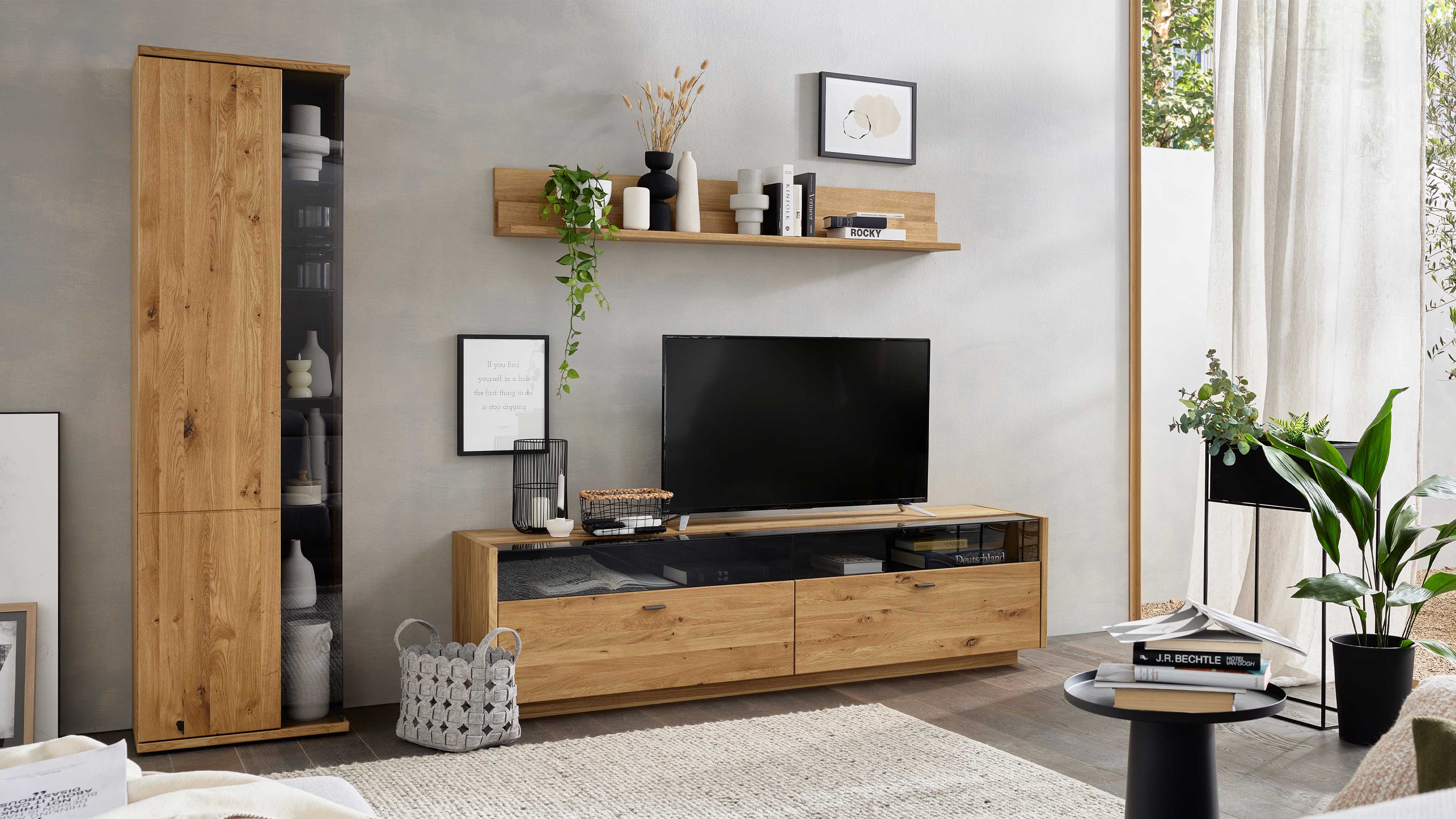 Wohnlösung mit TV-Board, hoher Vitrine und Wandregal mit grauen Glaselementen und Asteiche