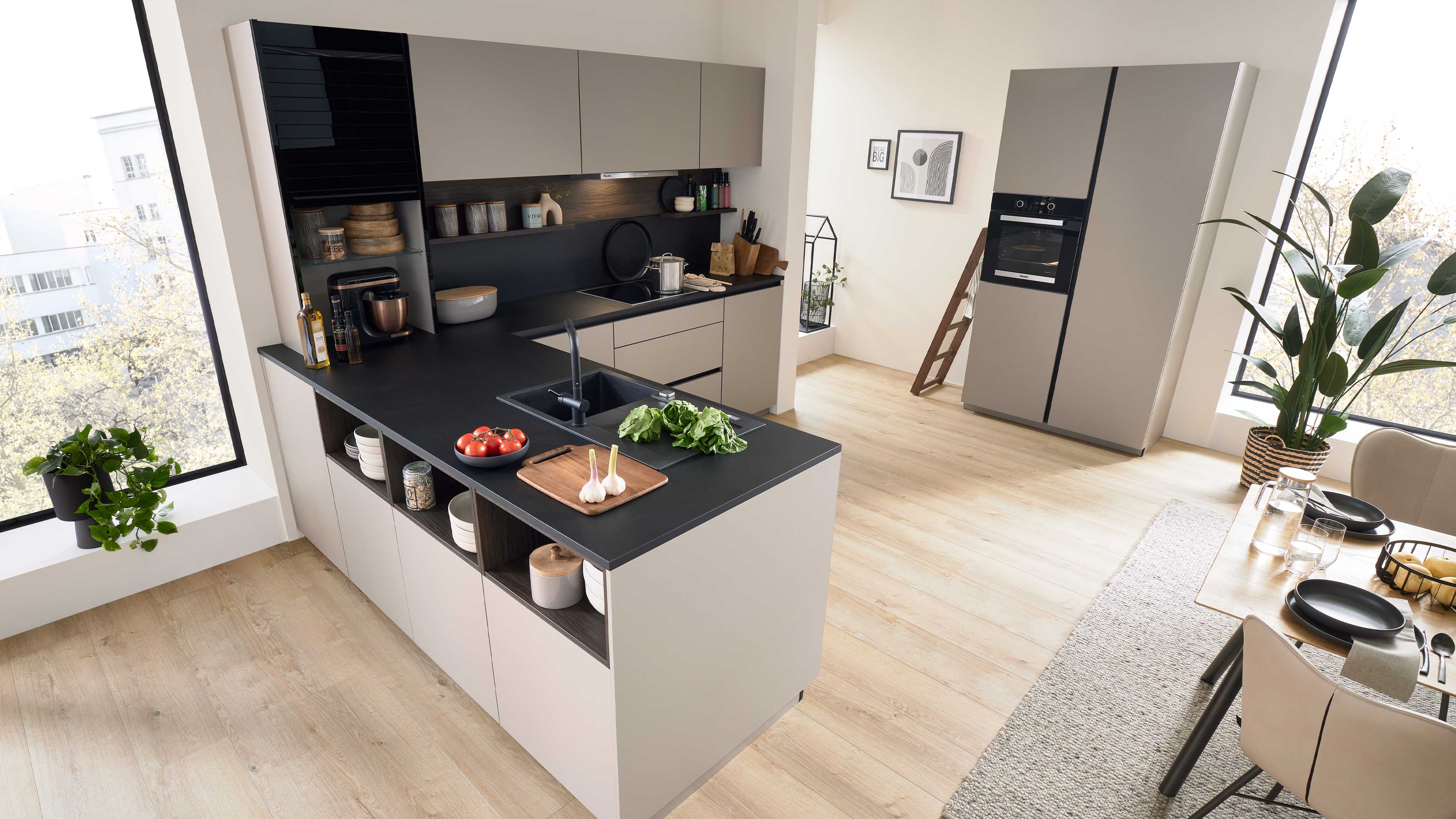 Küche mit Halbinsel und schwarzer Arbeitsplatte, Spüle, Schneidebrett mit Knoblauch und Tomaten, Hängeschränken und hohem Kühlschrank.