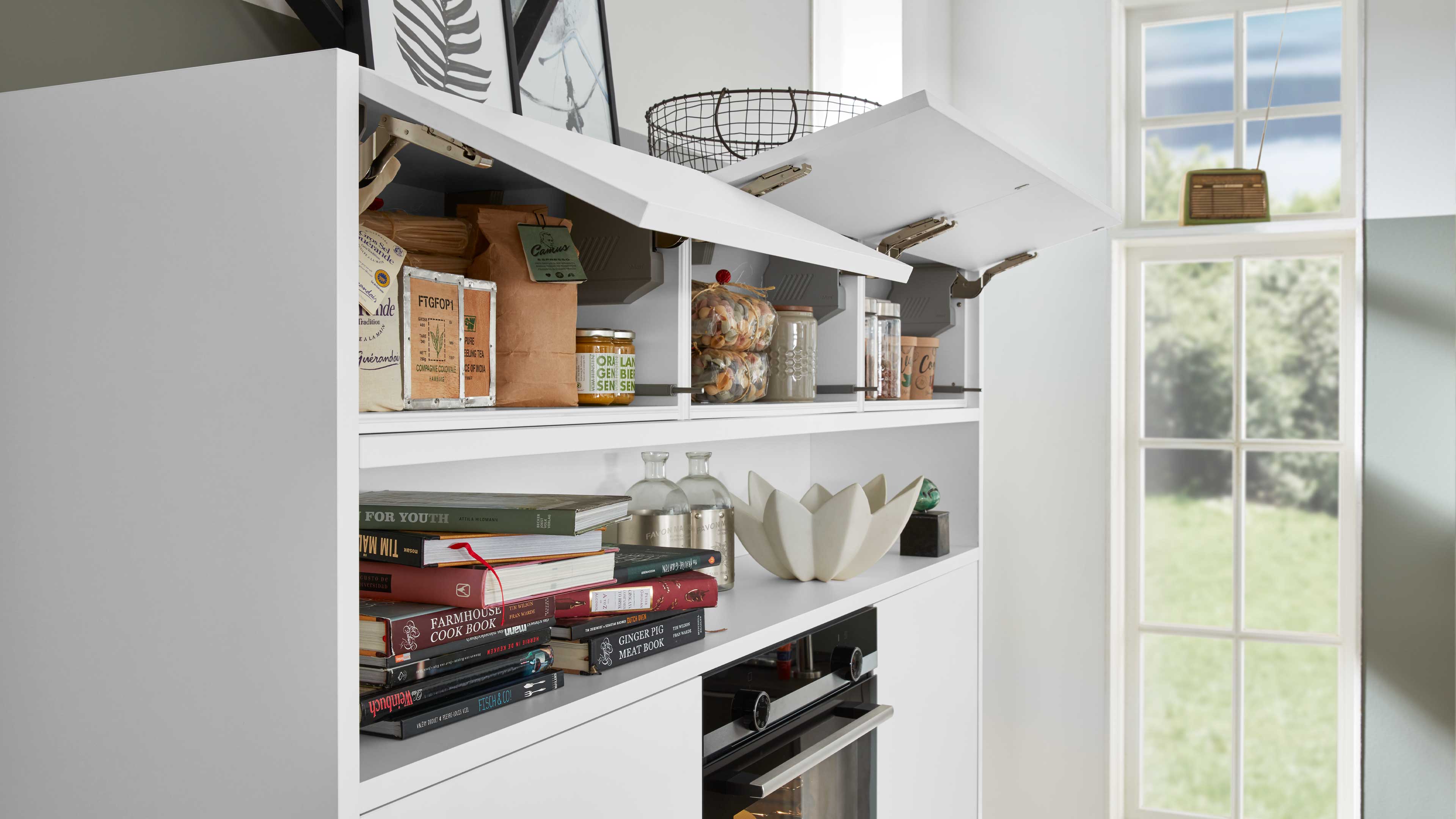 Weißer Küchenhochschrank mit drei aufklappbaren Fronten, offenen Regalfächern mit Gläsern, Vorratsdosen, Büchern und eingebautem Ofen.