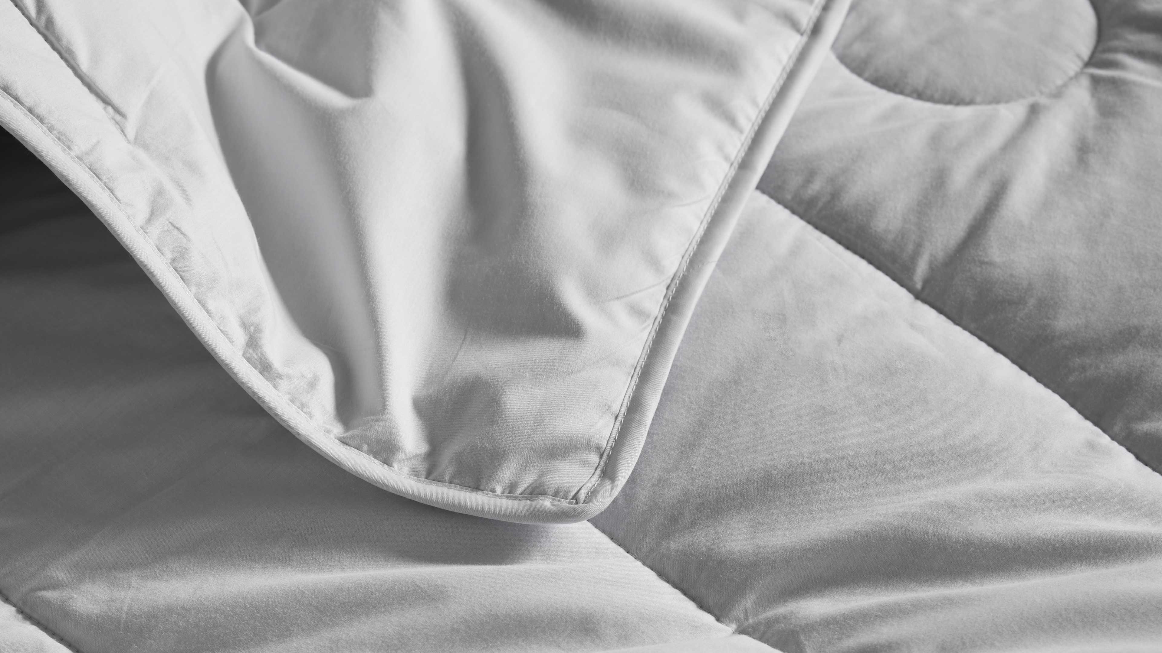 Gesteppte Bettdecke mit aufgeschlagener Kante, sichtbaren Nähten und gleichmäßigem, weichem Stoff.