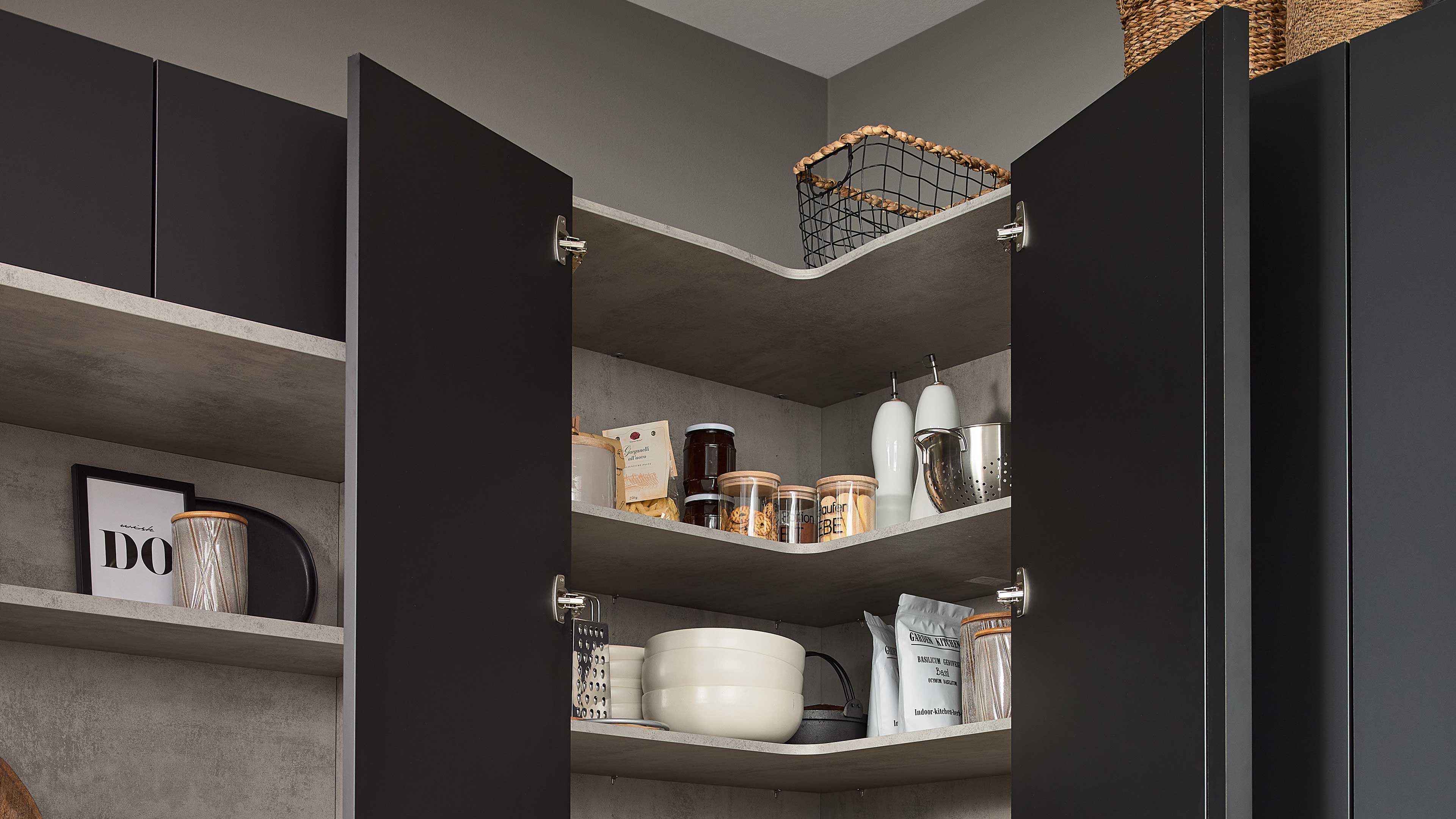 Offener Eckoberschrank mit geöffneten schwarzen Türen, grauen Innenschichten und Regalböden mit Vorratsgläsern, Schüsseln und Deko.