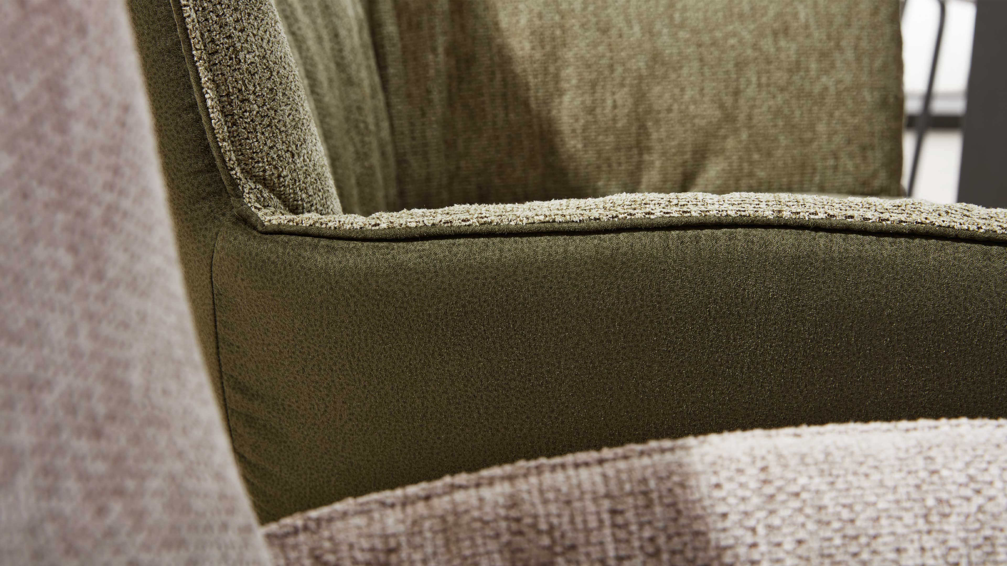Nahaufnahme eines olivgrünen Sesselarms mit sichtbarer Kante und Vordergrund aus hellbeigem, grob gewebtem Stoff.