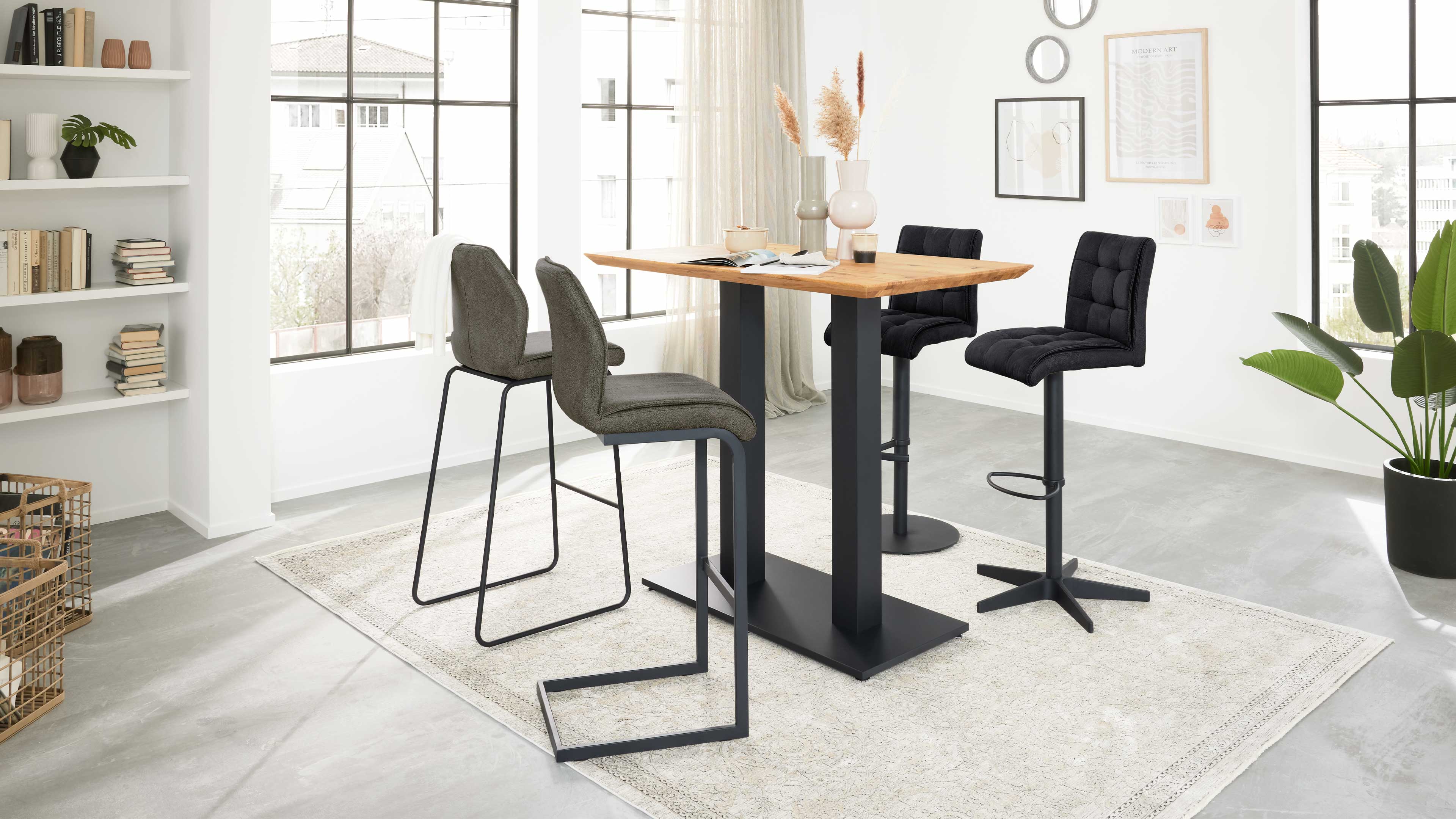 Rechteckiger Hochtisch mit Holzplatte auf schwarzem Metallgestell, zwei graue Schlittensitze links, zwei schwarze Hocker rechts.