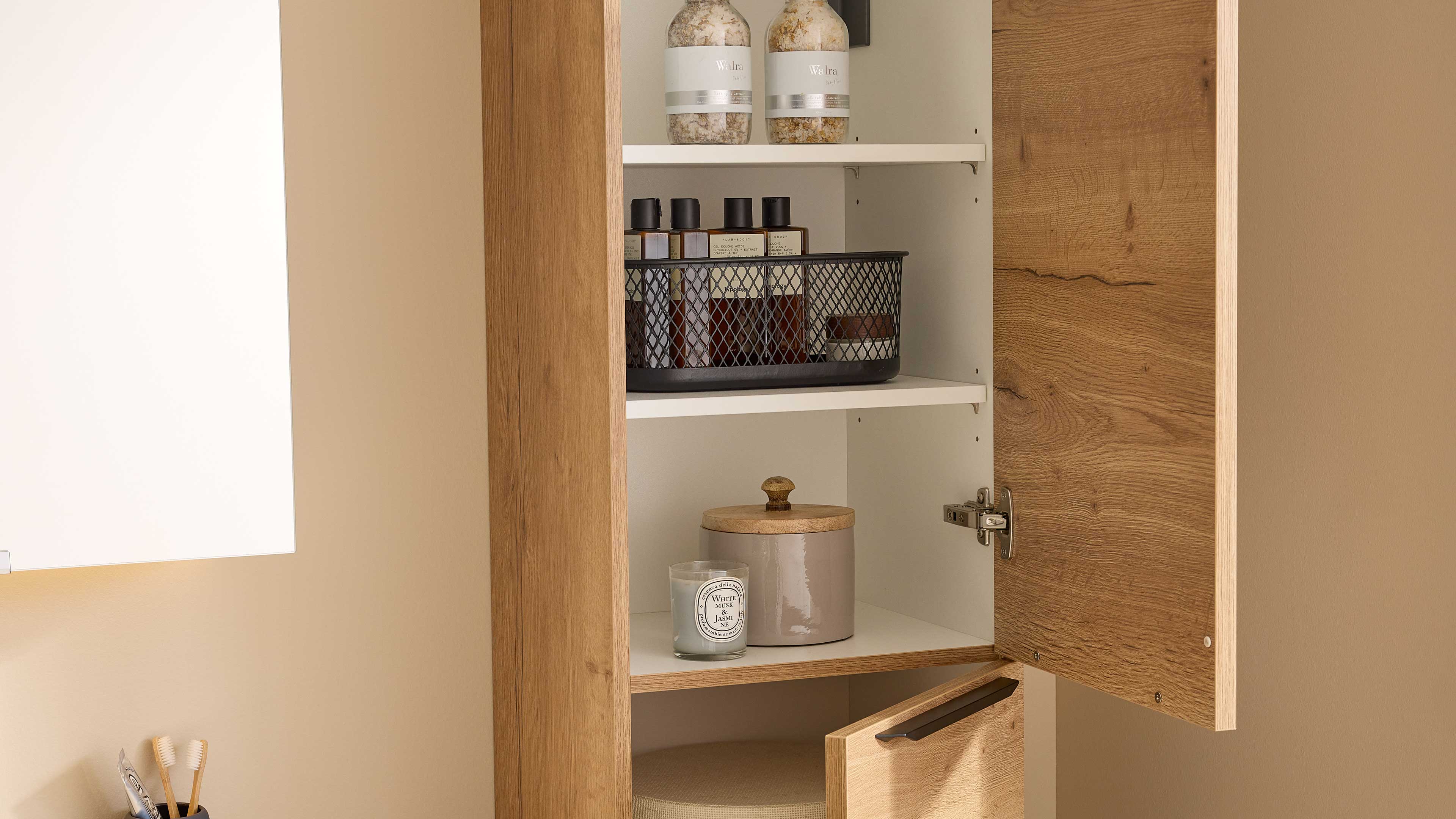 Hängender Holzschrank mit geöffneter Tür, innen weiße Regalböden, Metallkorb mit Flaschen, Kerze und Dose.