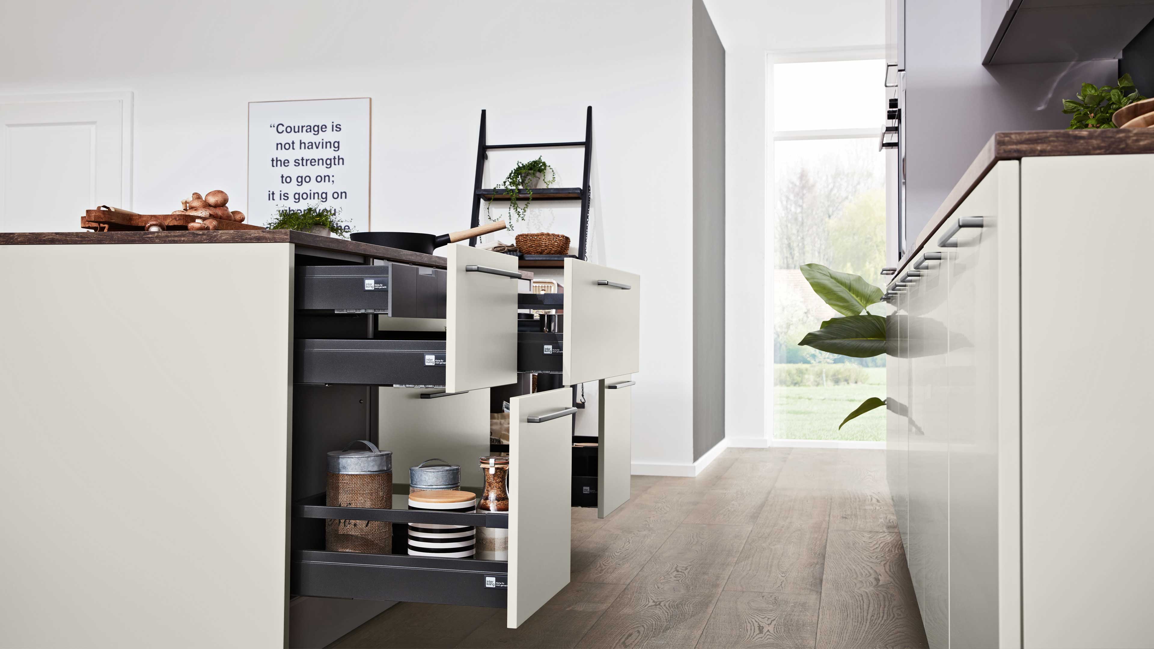 Kücheninsel im Vordergrund mit mehreren geöffneten Schubladen und schwarzen Innenauszügen, Holzarbeitsplatte, Dosen und Regal im Hintergrund.