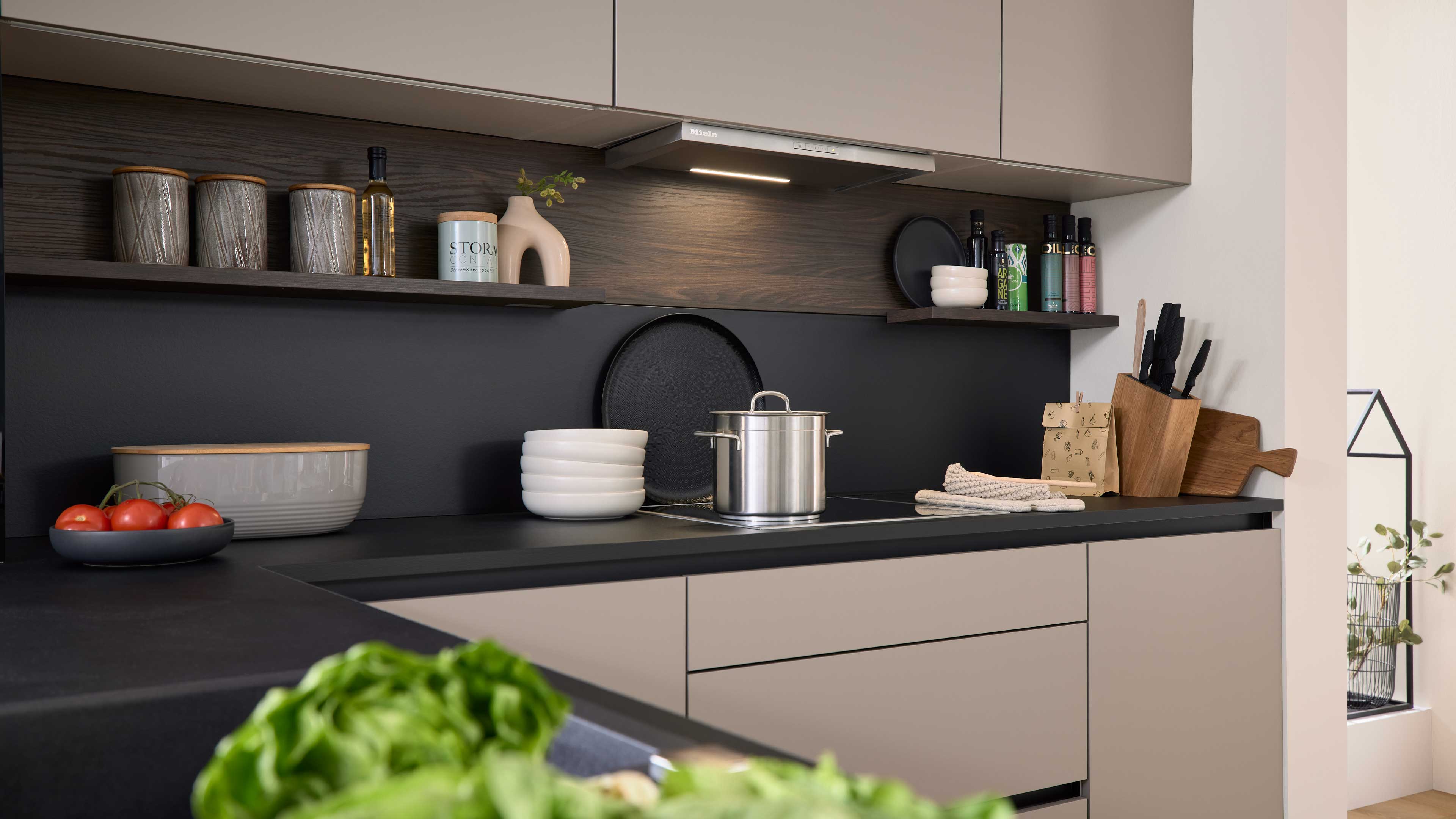 Küchenarbeitsplatte mit Edelstahltopf auf Induktionsfeld, gestapelten weißen Schalen, Messerblock, Schneidebrettern und Regalen.