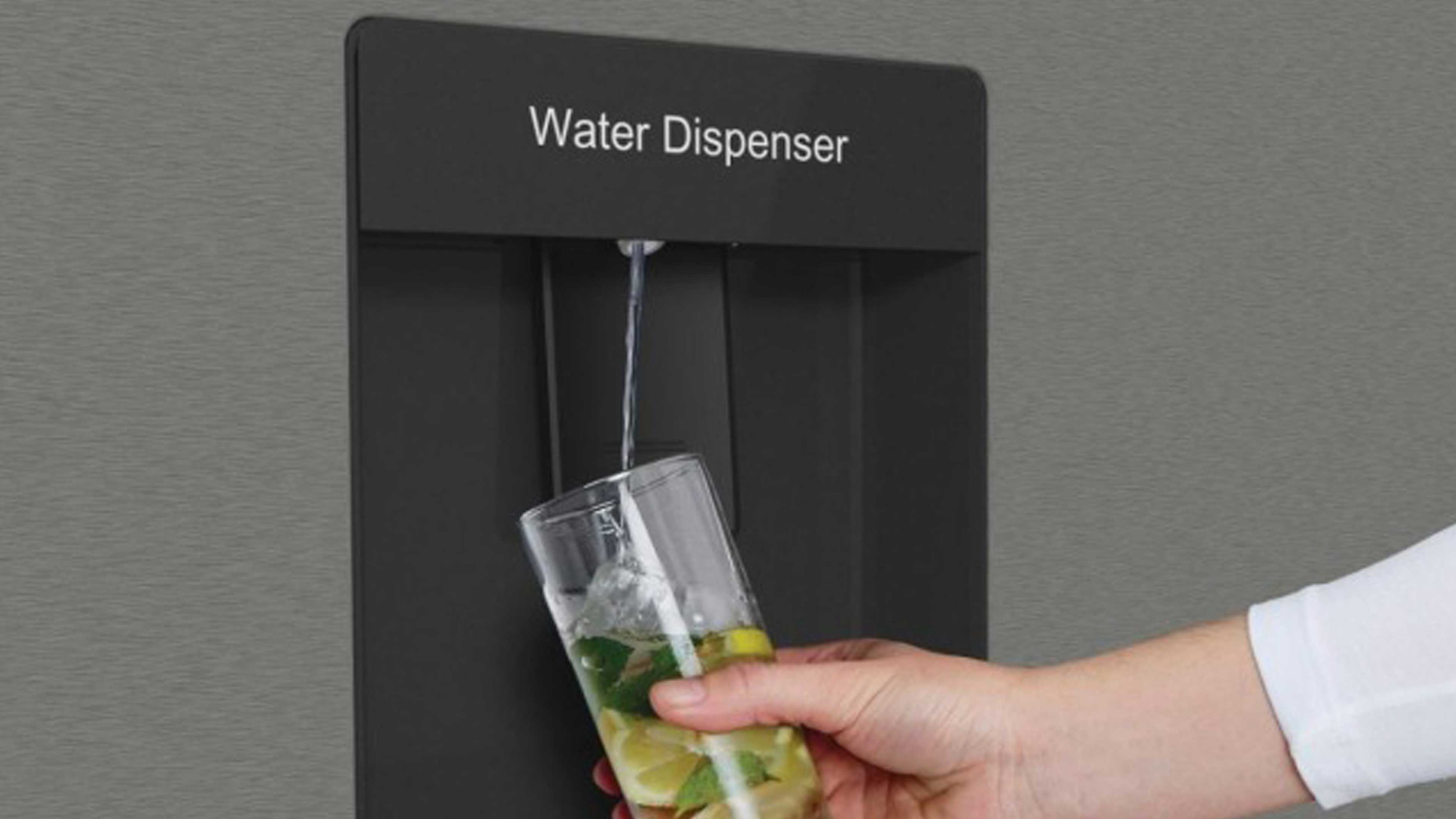 Schwarzer Water Dispenser mit laufendem Wasserstrahl, ein Glas mit Eis, Zitronenscheiben und Minzblättern wird von einer Hand gehalten.