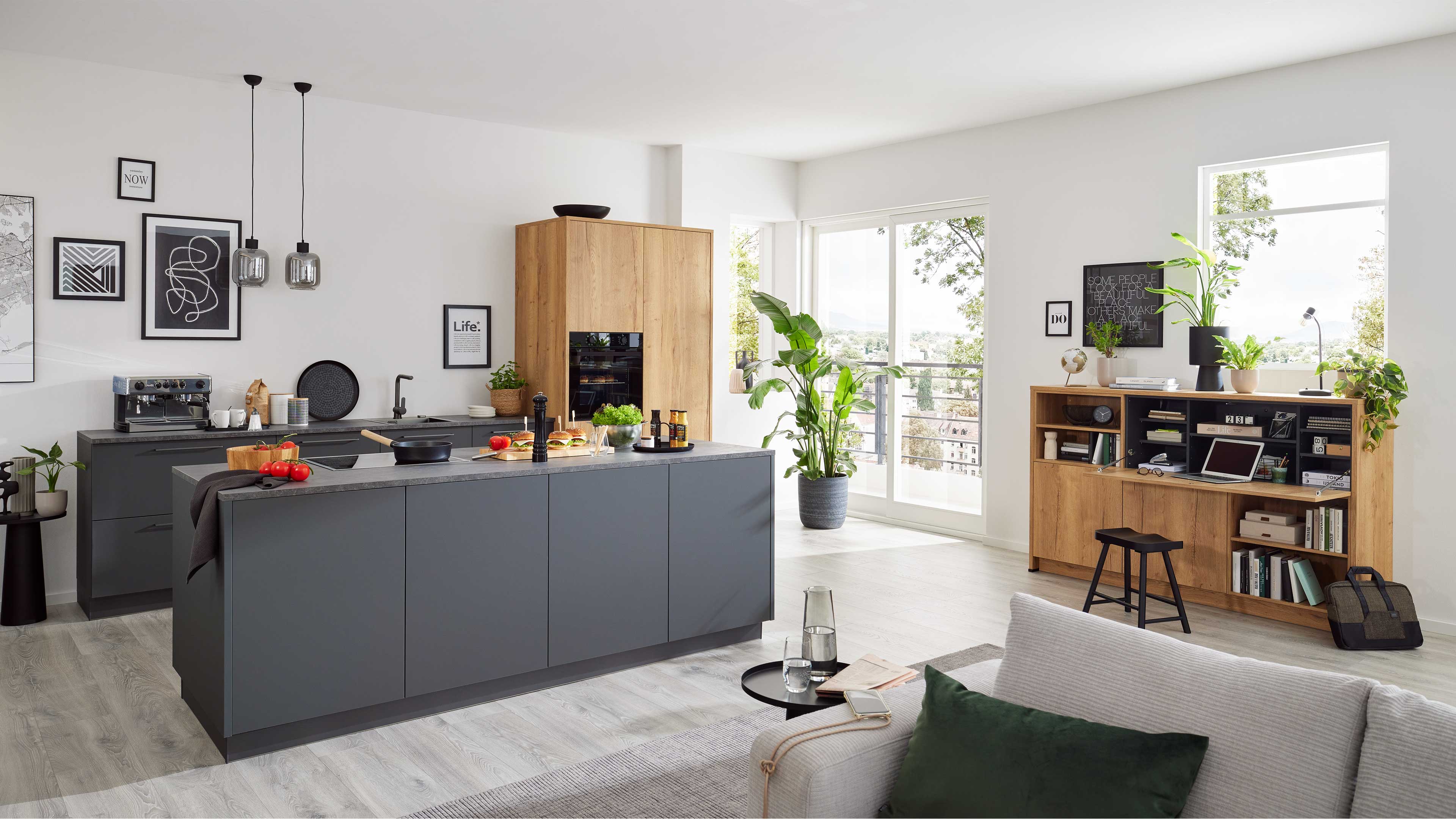 Matte dunkelgraue Kücheninsel mit Kochfeld und Holzarbeitsplatte, links graue Unterschränke, rechts hoher Holzschrank und Regal.