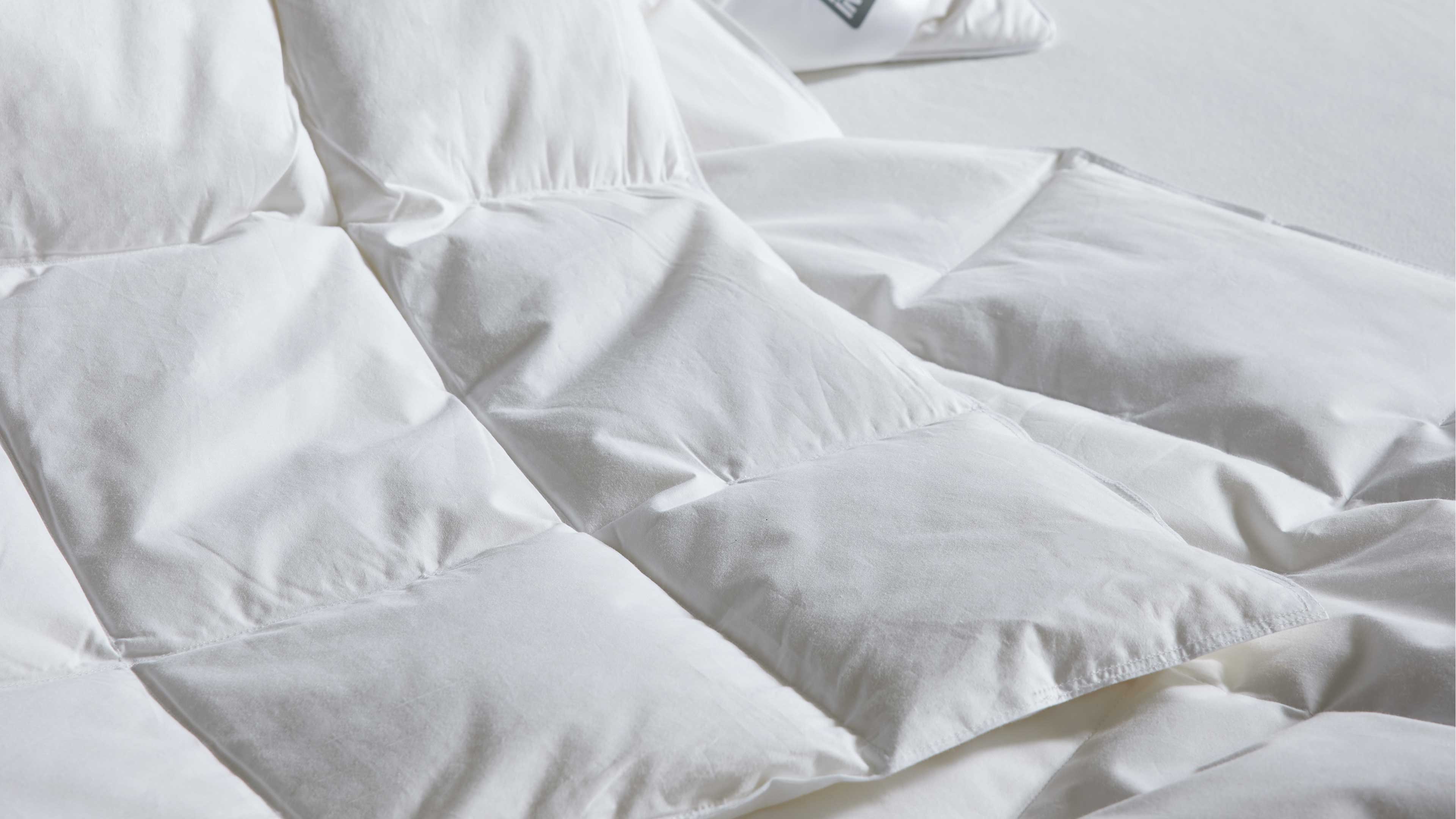 Weiße gesteppte Bettdecke mit großen quadratischen Kammern, Nahaufnahme zeigt gepolsterte, leicht gewellte Oberfläche.