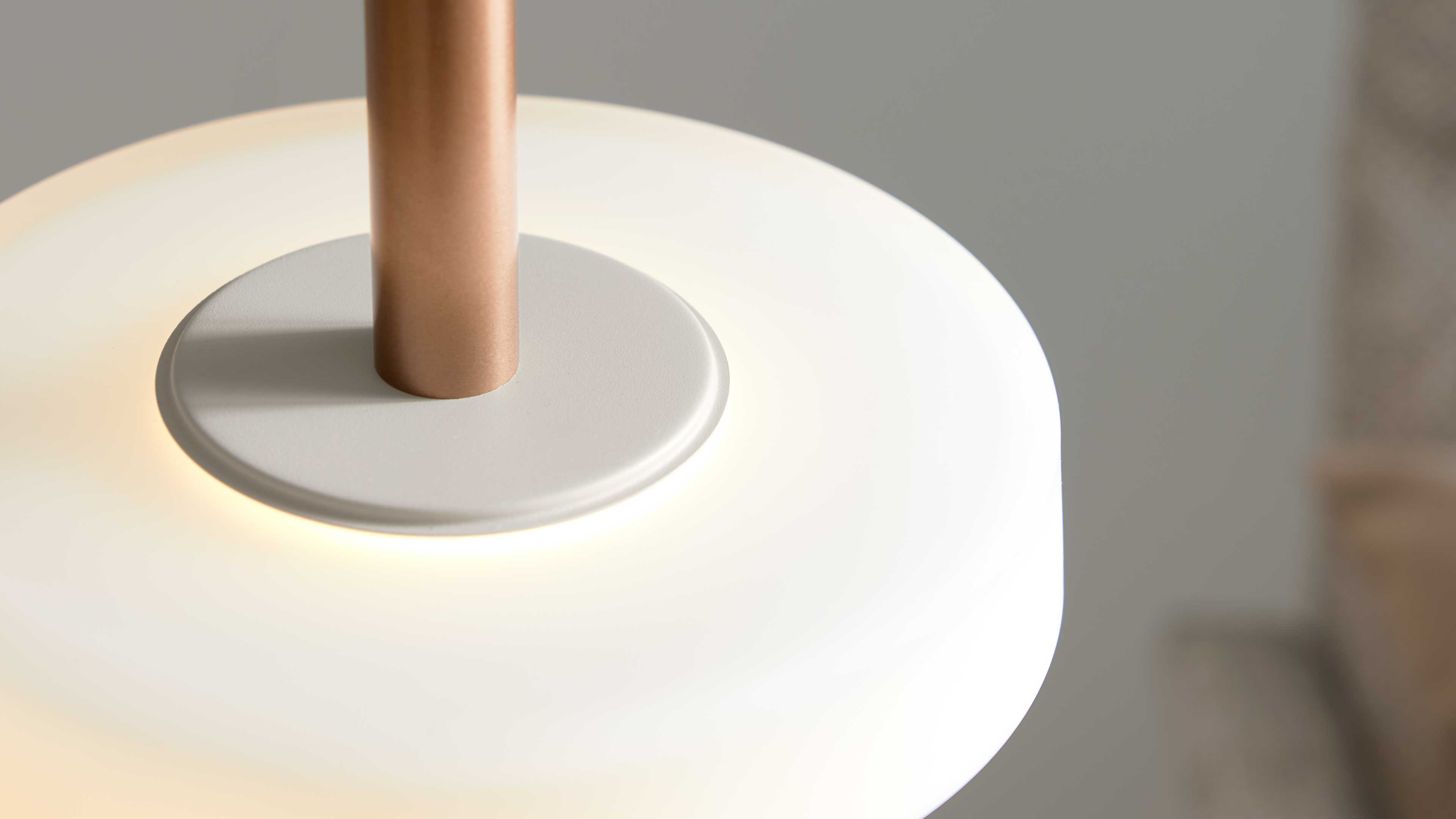 Runde weiße Pendelleuchte mit Metallstange in Roségold und kleiner weißer Befestigungsplatte, warm beleuchtet.