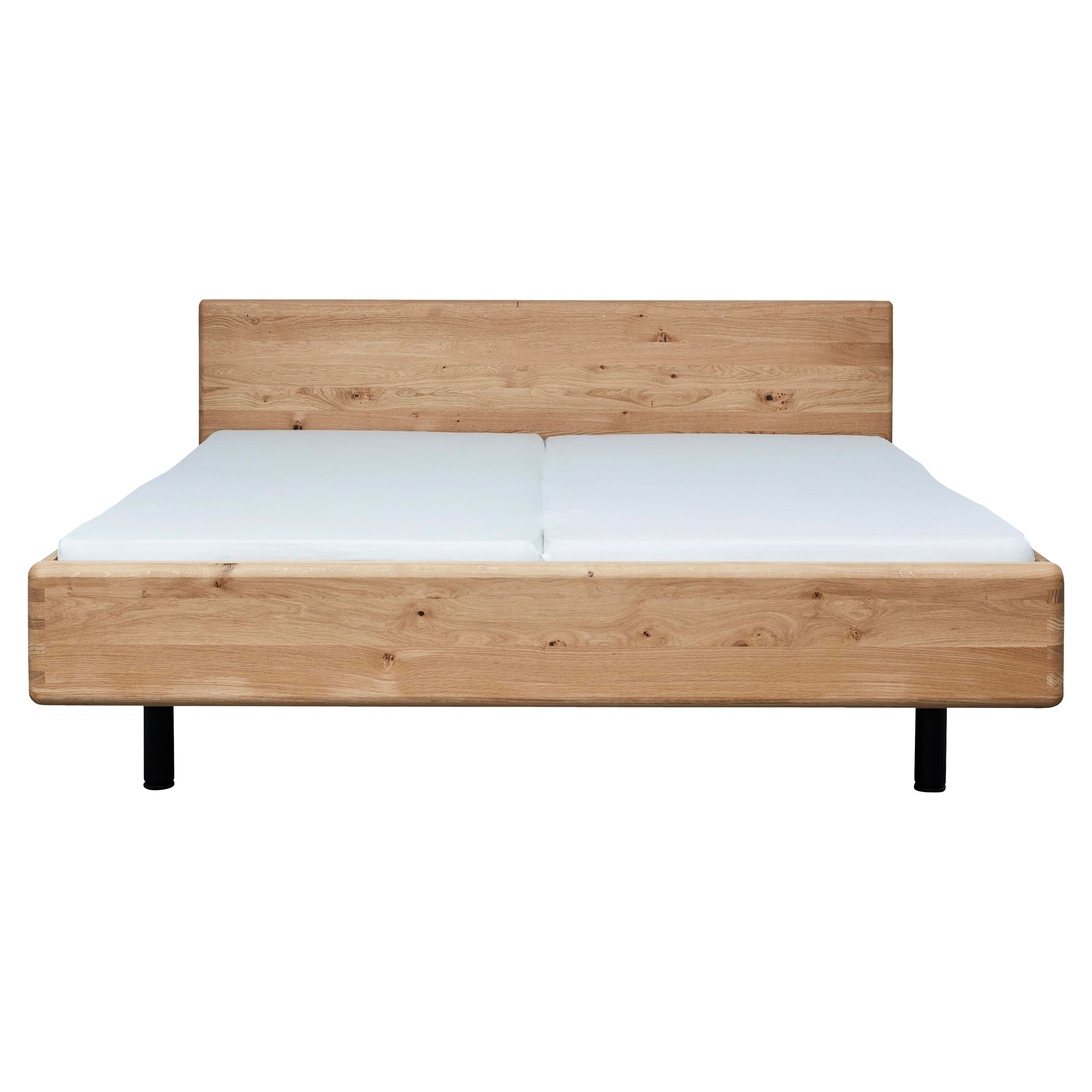 Bettgestell aus hellem Holz mit sichtbaren Ästen und Kopfteil, zwei weiße Matratzen und schwarze runde Beine.