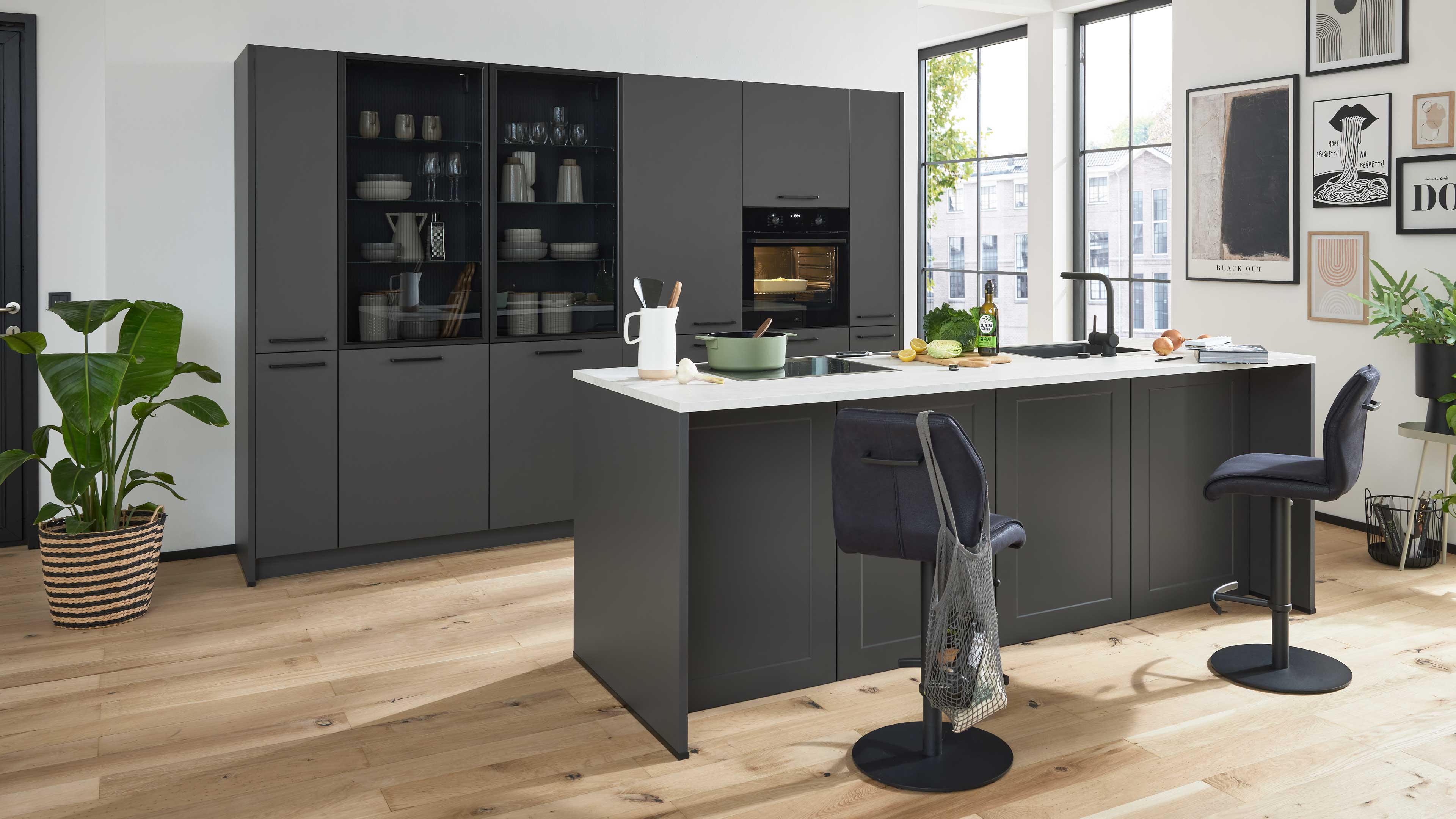 Dunkelgraue Kücheninsel mit weißer Arbeitsplatte, zwei Barhockern, eingelassenem Kochfeld und angrenzenden Hochschränken.