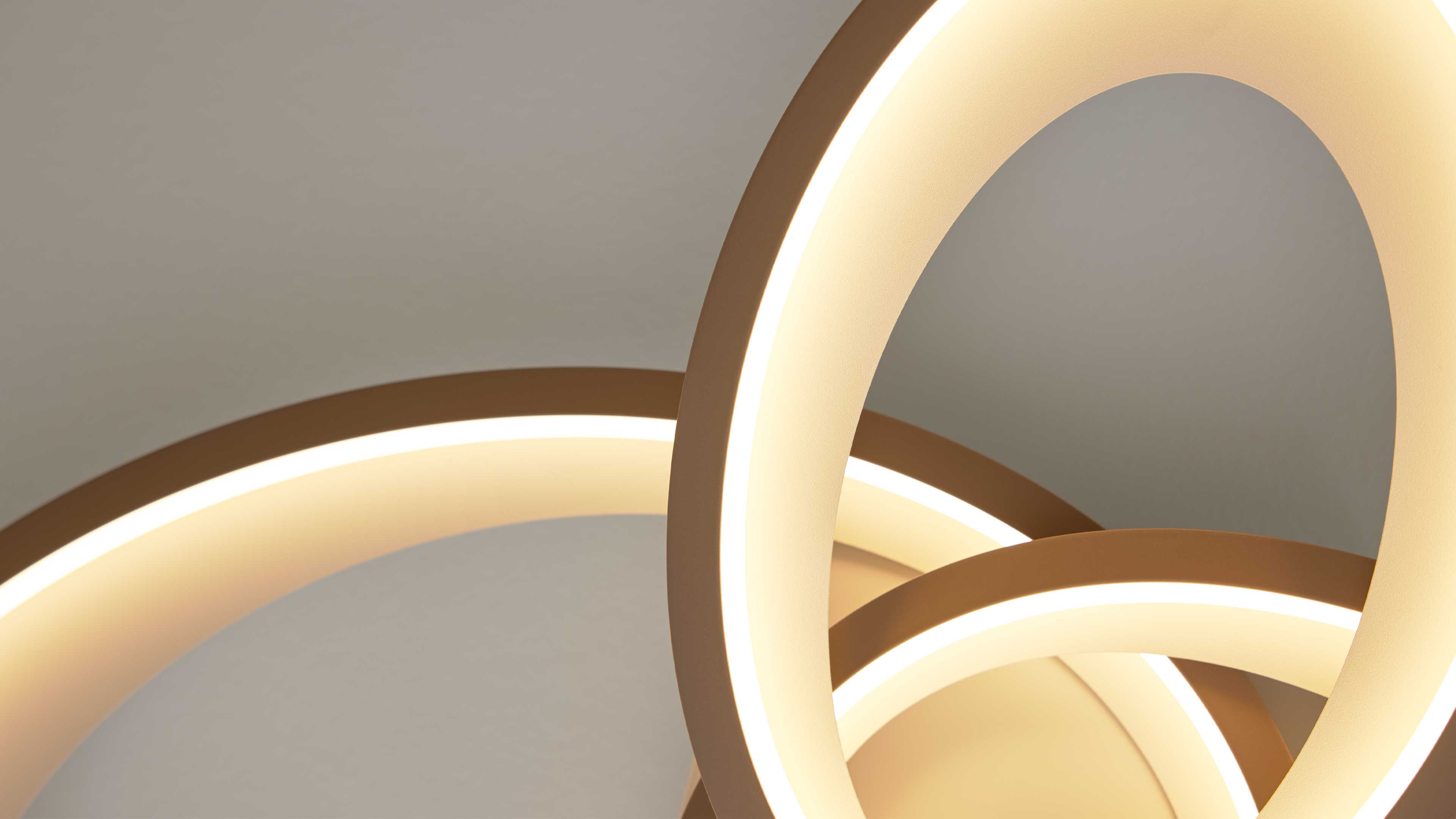 Mehrere überlappende, beleuchtete Ringleuchten in warmweiß mit goldfarbenen Rahmen vor neutraler Decke.