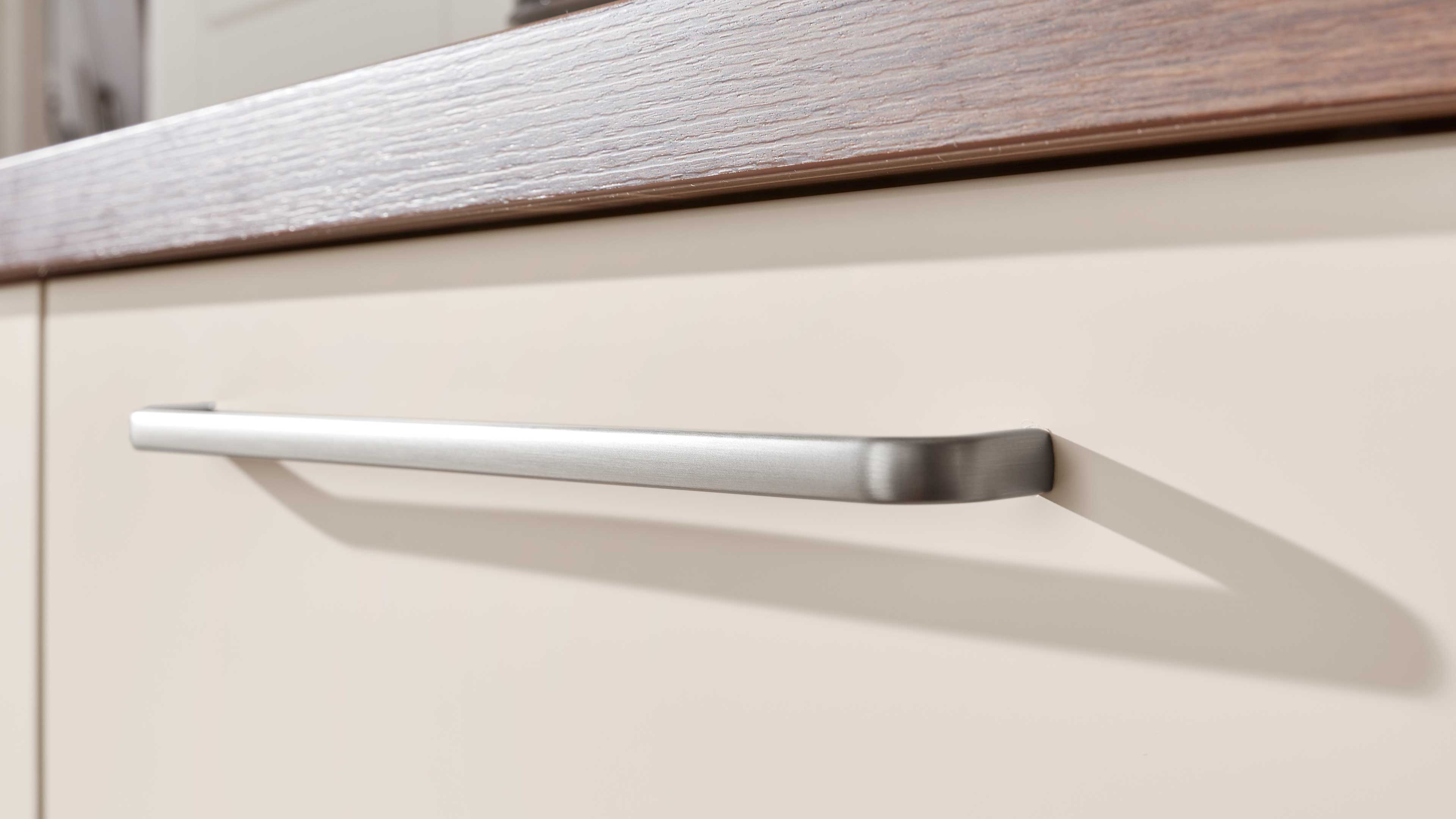 Nahaufnahme einer hellbeigen Schubladenfront mit langem, gebürstetem Metallgriff und sichtbarer Holzkante oben.