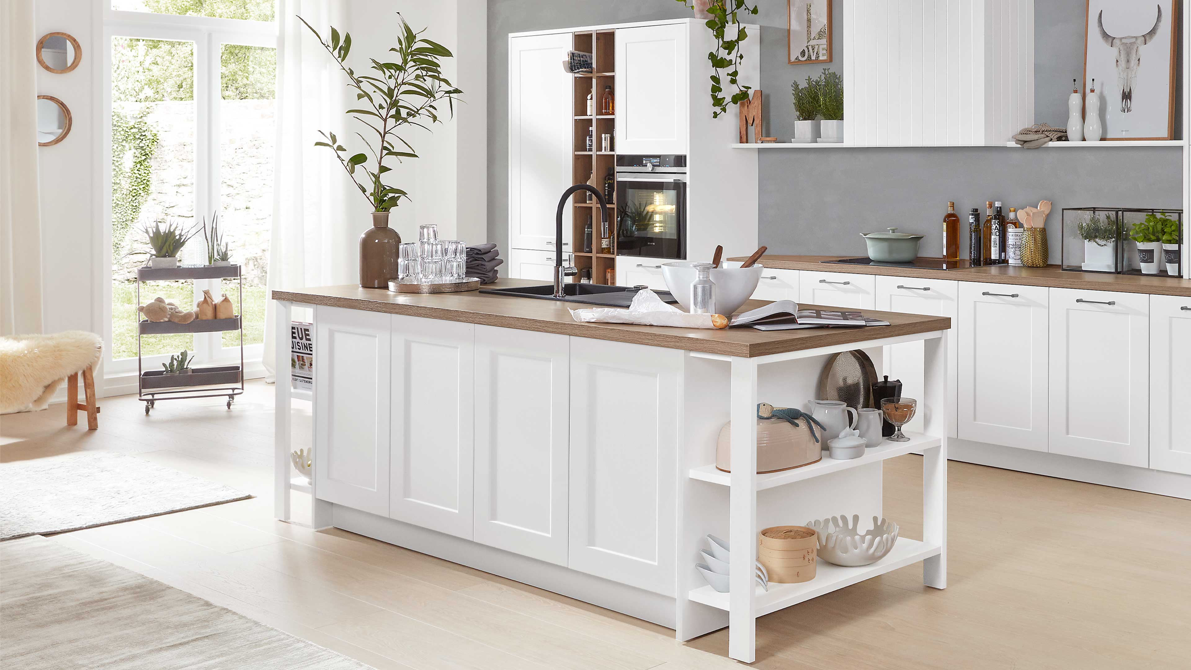 Kücheninsel mit weiß lackierten Rahmenfronten, Holzarbeitsplatte, eingelassenem Spülbecken und offenem Regal.
