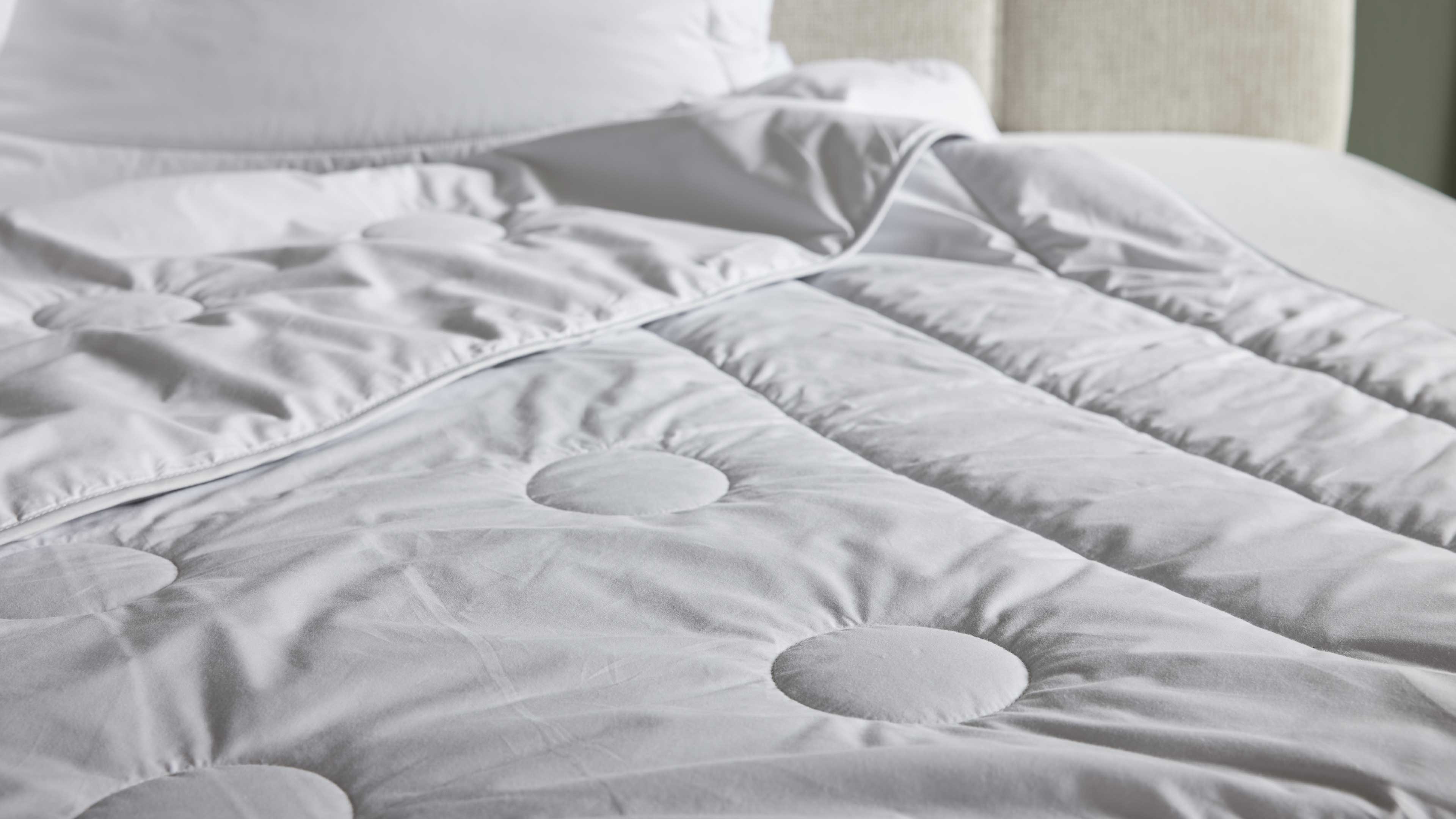 Weiße gesteppte Bettdecke mit kreisförmigen Steppungen und leicht umgeschlagener Kante auf Matratze.