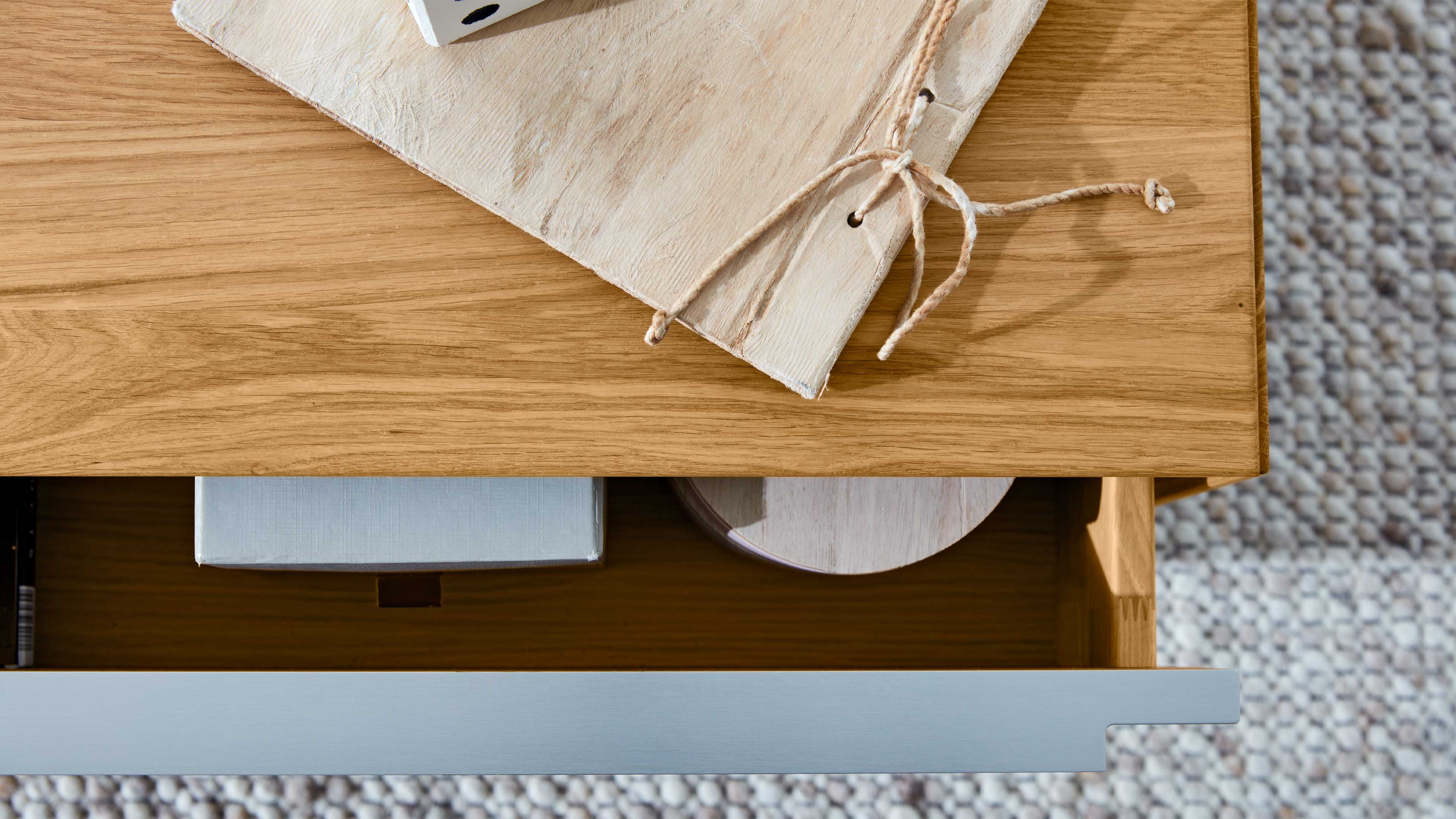 Holztisch mit geöffnetem Schubfach, darauf ein helles Holzbrett mit gebundener Schnur, im Fach Box und runde Dose.