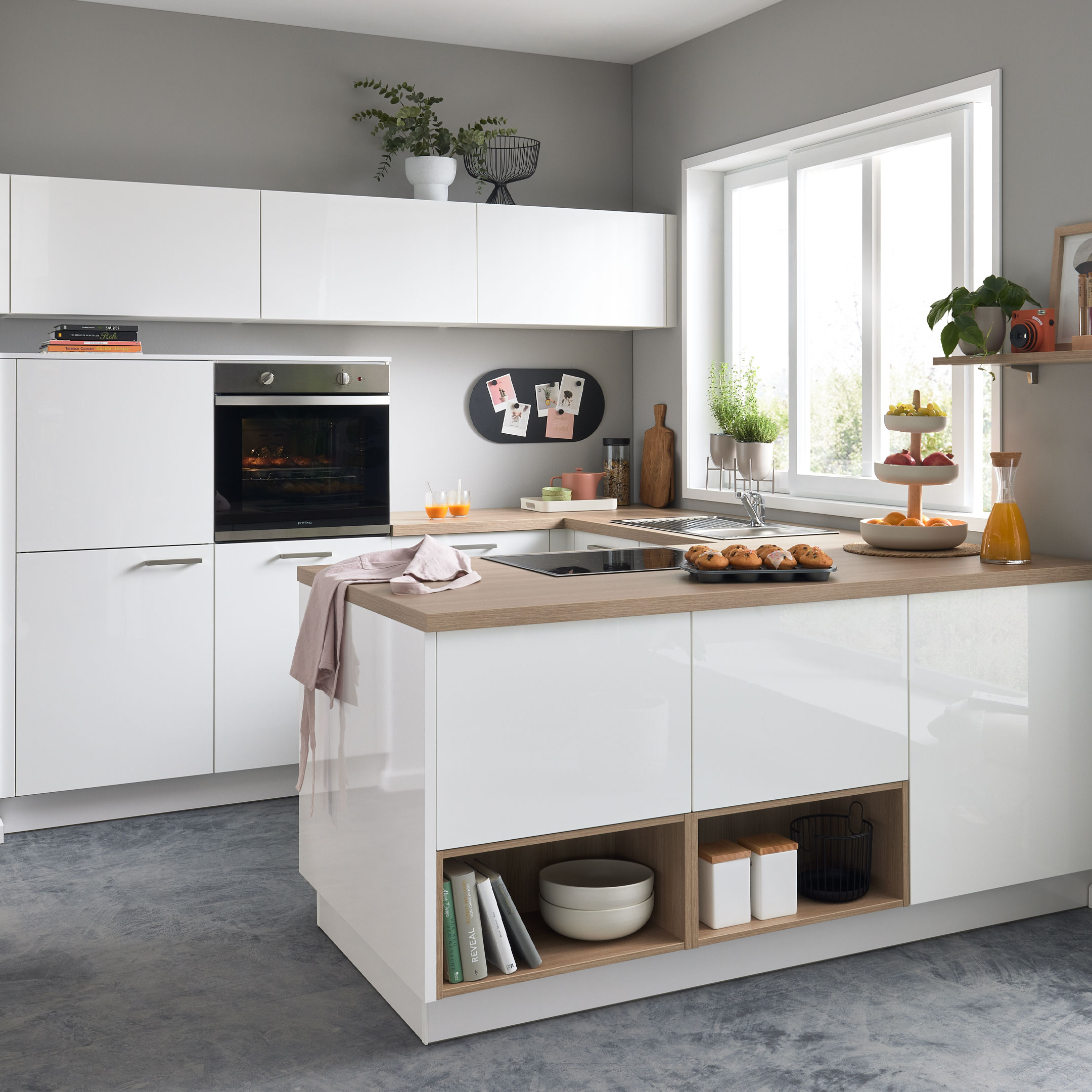 Weiße Kücheninsel mit Holzarbeitsplatte, eingebautem Kochfeld und offenen Fächern, daneben Hochschrank mit Ofen und Fensterbank.