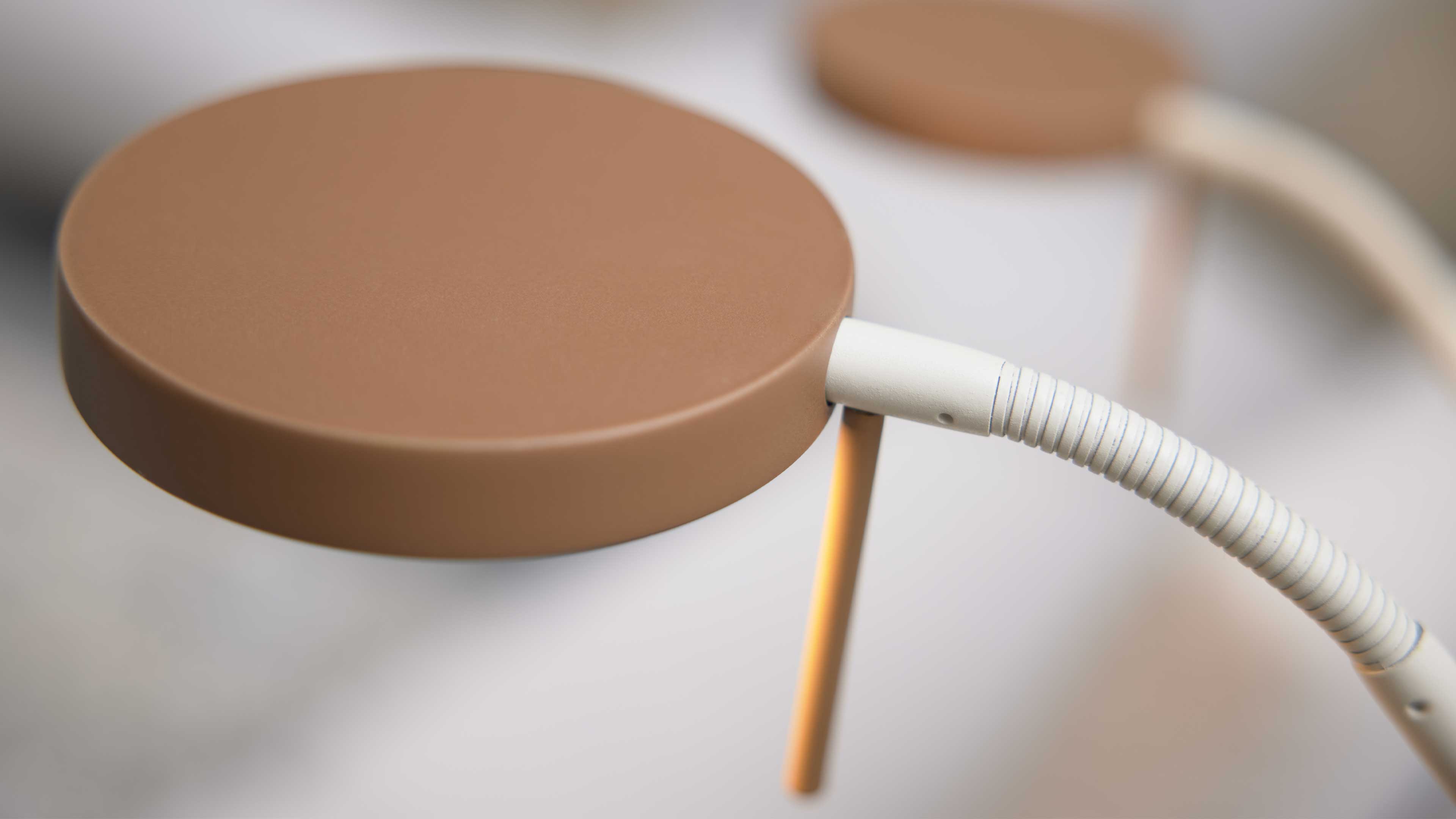Großaufnahme einer runden braunen Lampenleuchte mit weißem geripptem Flexarm und dünnem orangefarbenem Stab.