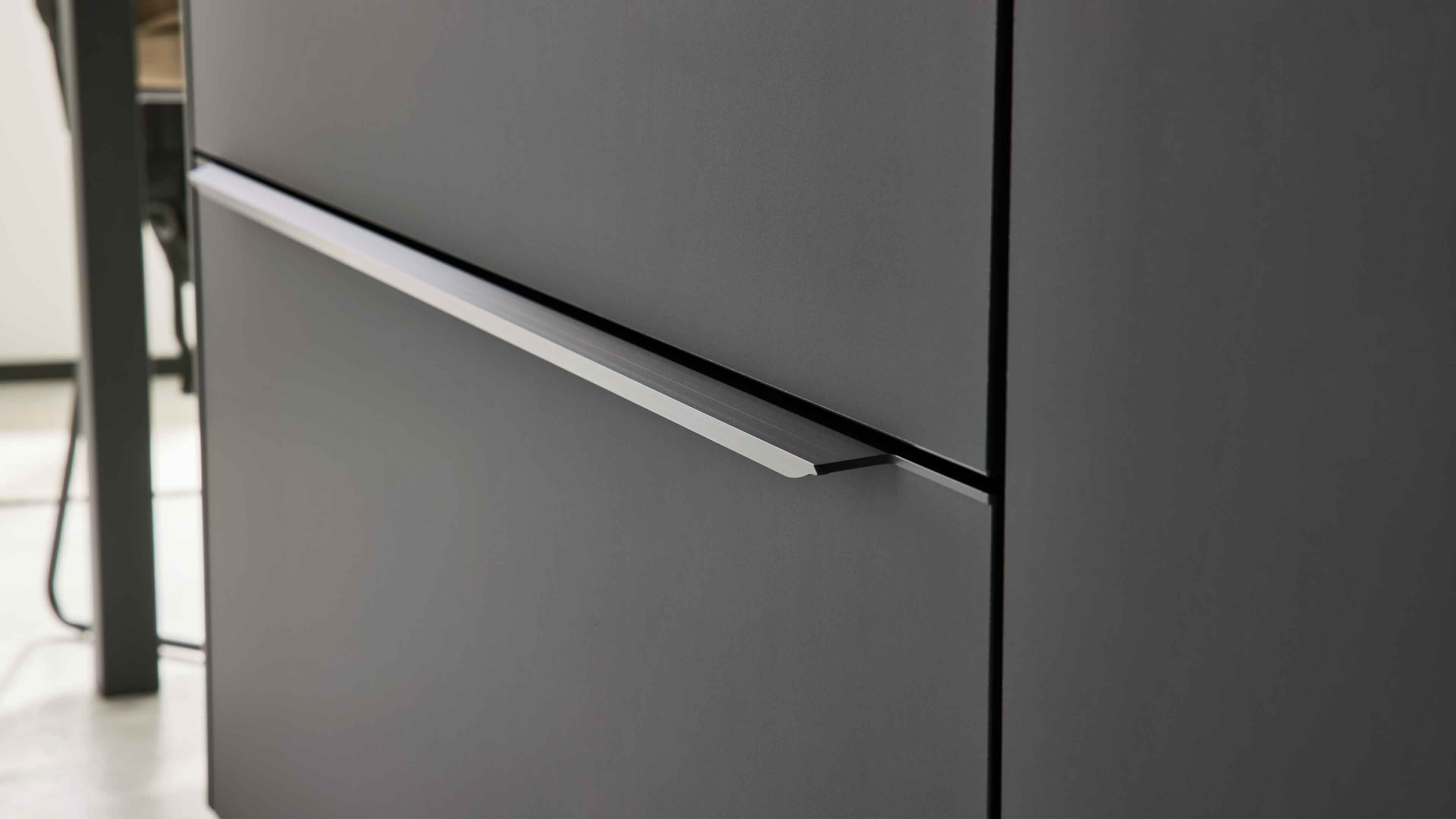 Nahaufnahme einer dunkelgrauen Schubladenfront mit schmalem silbernem Griffprofil im Spalt zwischen zwei Schubladen.