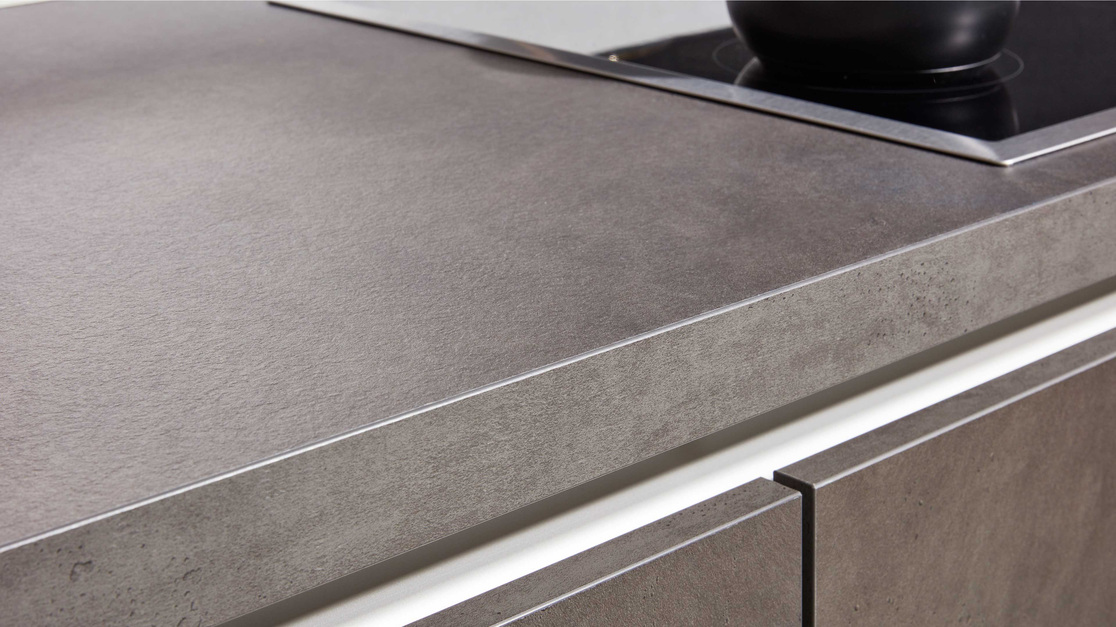 Grau strukturierte Küchenarbeitsplatte mit sichtbarer Kante, bündigen Schubladenfronten und teilweisem Glaskeramikfeld.