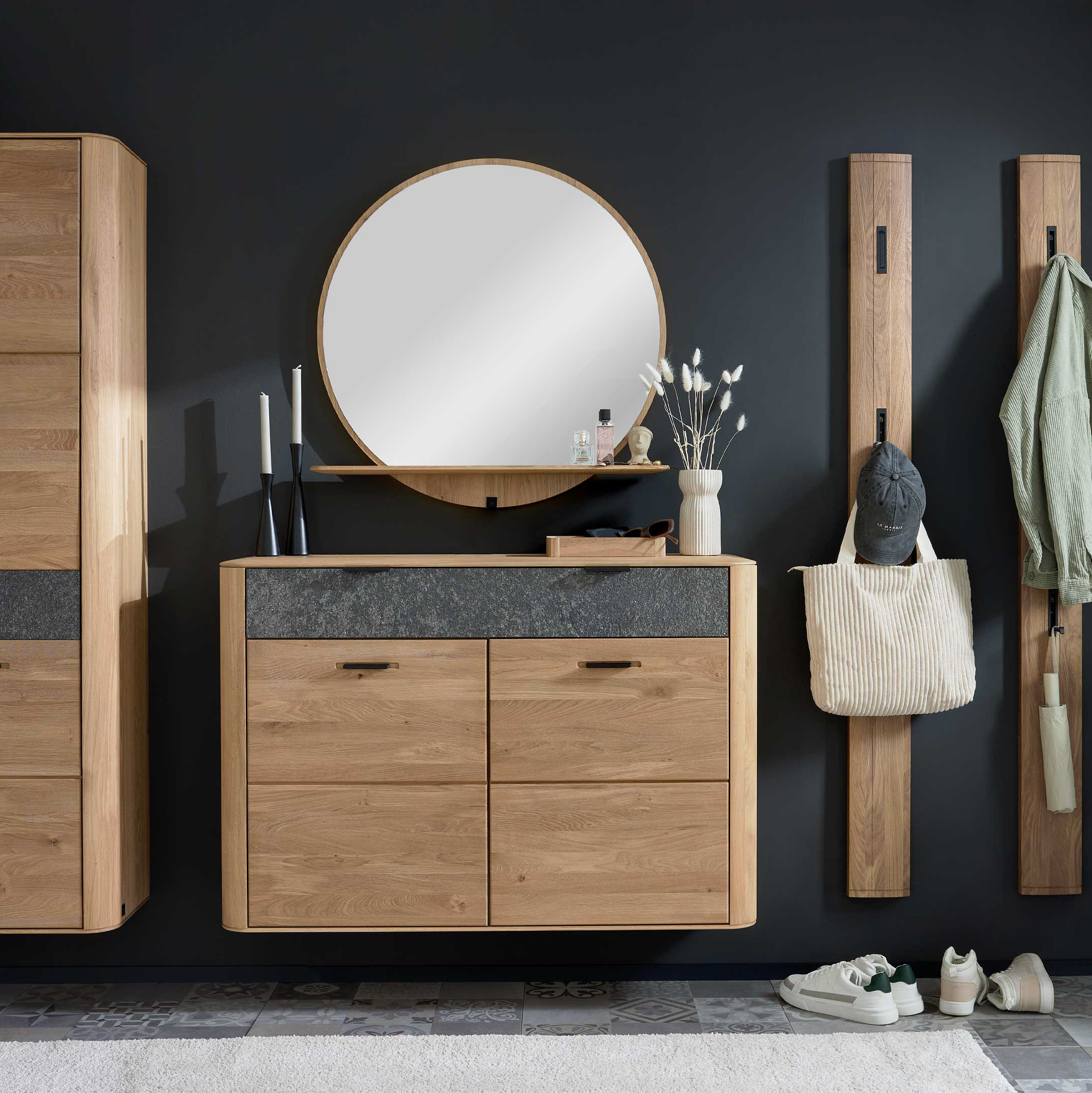 Wandhängende eichefarbene Kommode mit rundem Spiegel und Ablage, links hoher Schrank, rechts zwei Holz-Hakenleisten, Pflanzen und Schuhe.