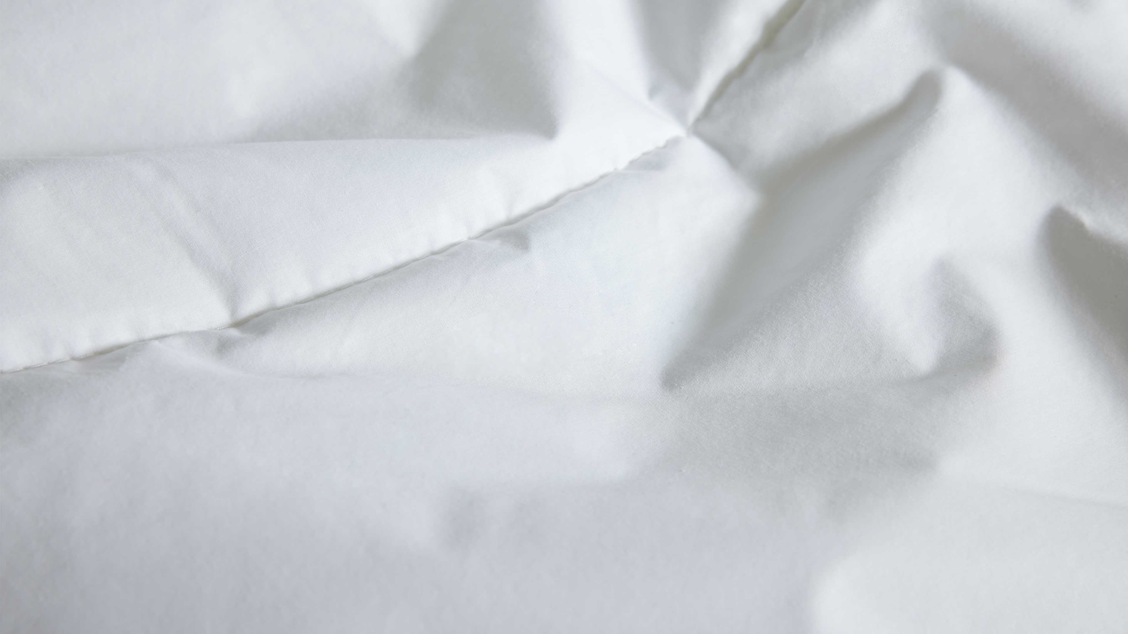 Weiße Bettdecke mit sichtbarer Steppnaht und weichen Falten, Nahaufnahme der glatten Oberfläche.