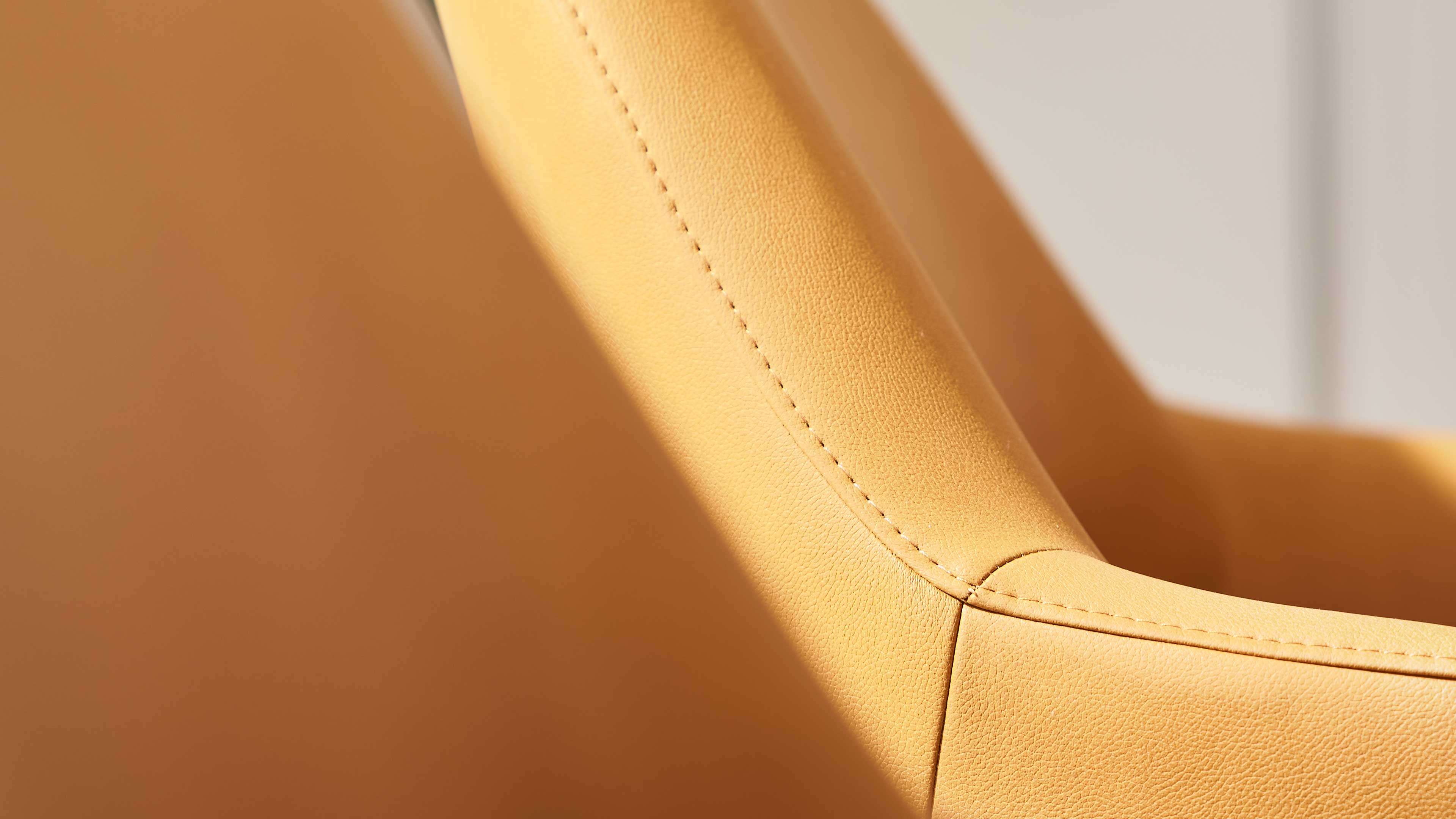 Gelb-orange Polsterfläche eines Stuhls mit feiner Narbung und sichtbaren Ziernähten an Rückenlehne und Armlehne.