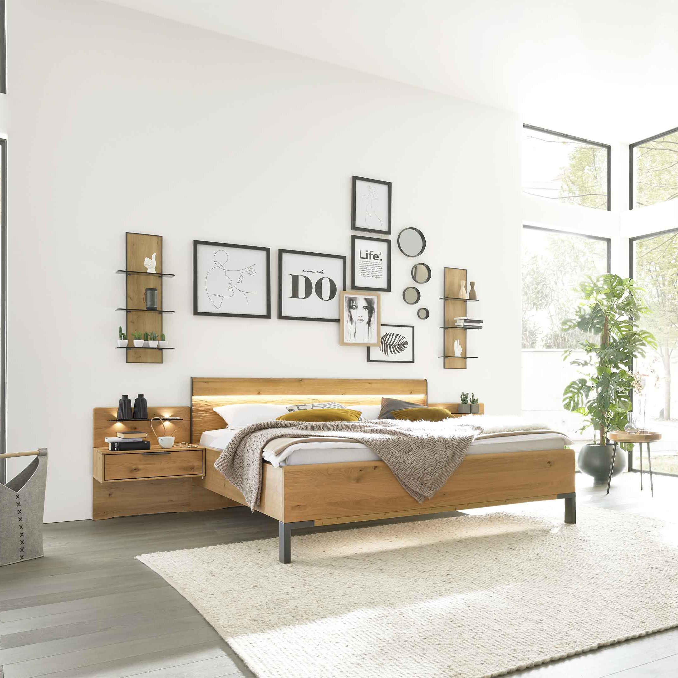 Holzbett mit Nachttisch, hellen Textilien und Wandbildern, daneben großer Schiebetürenschrank mit Holzpaneel und Beleuchtung.