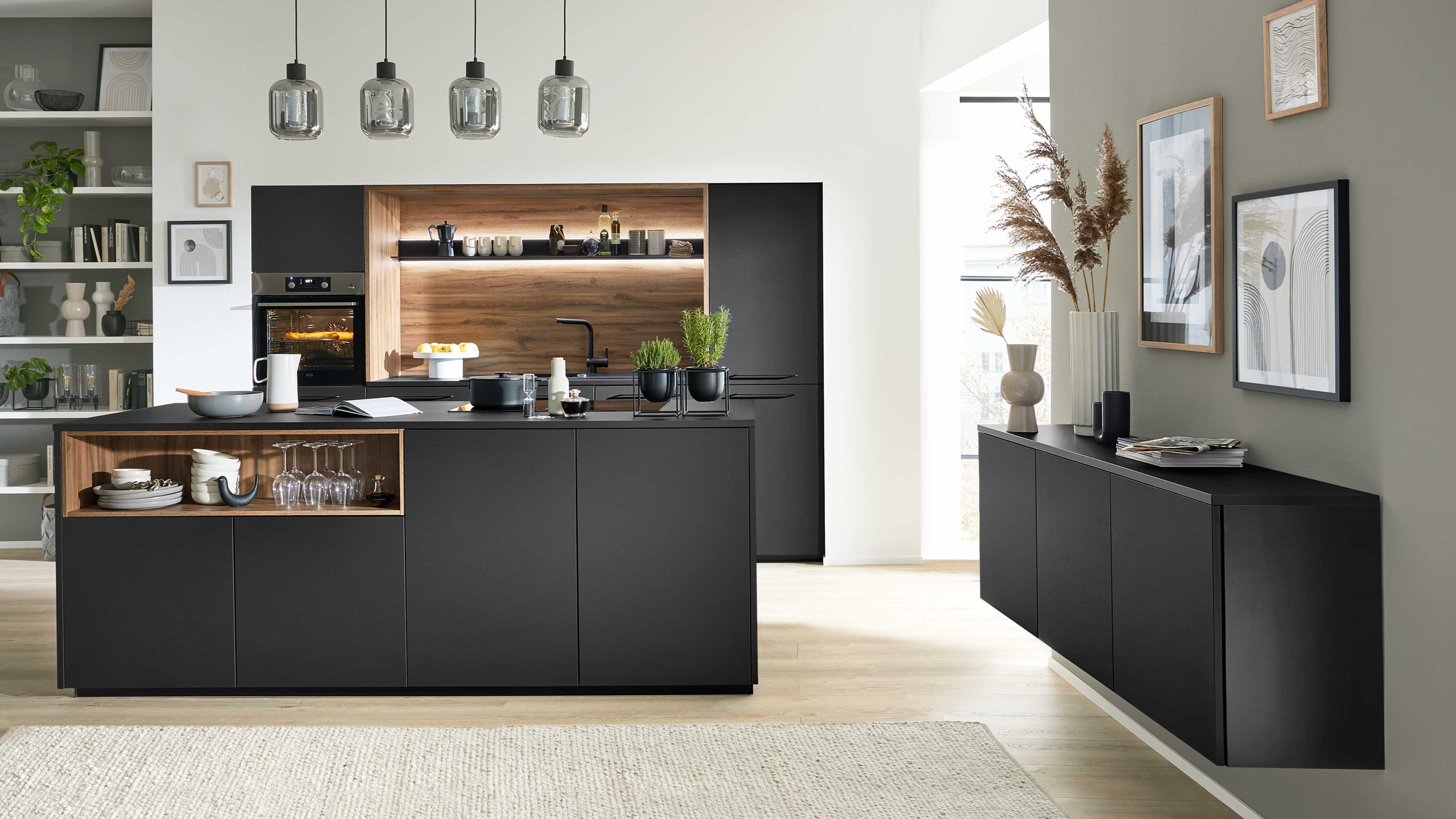 Schwarze Kücheninsel mit offenem Holzfach, eingebautem Backofen und Holzrückwand, hängenden Glaslampen und seitlichem Sideboard.