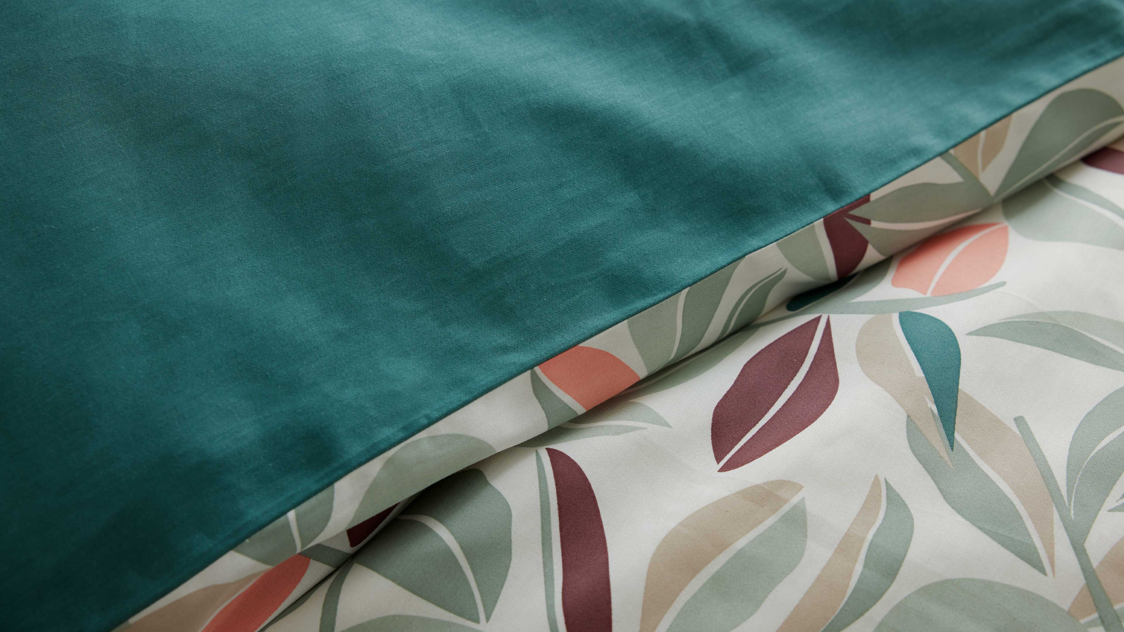 Bettwäsche, oben glatter petrolgrüner Stoff, darunter weißer Stoff mit pastellfarbenem, organischem Blattmuster.