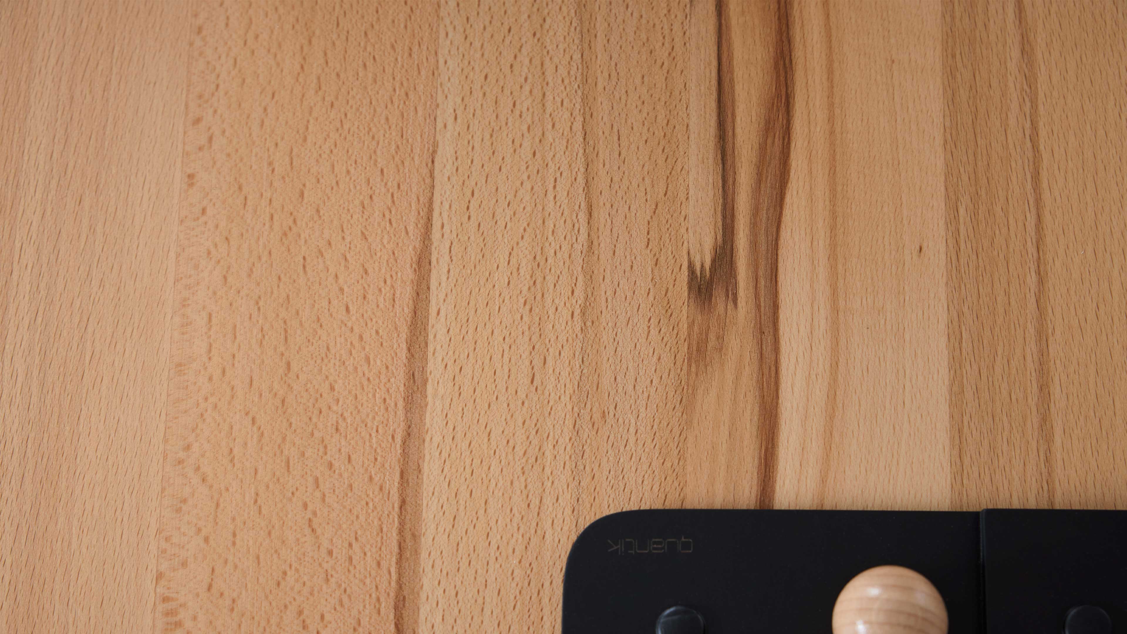 Helle Holzfläche mit senkrechter Maserung und rechts unten ein schwarzes Wandhakenstück mit rundem hellen Holzknauf.