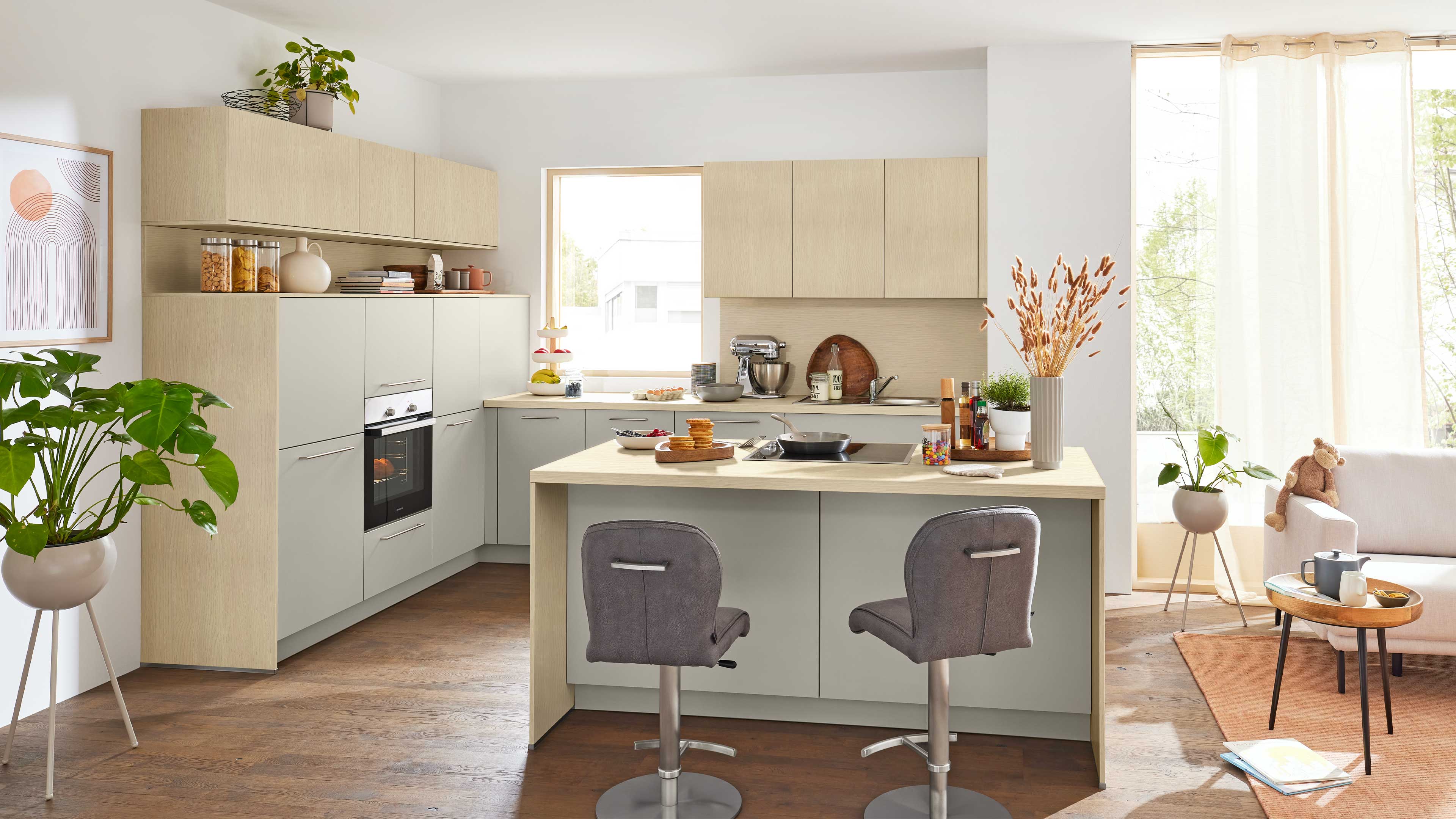 Offene Wohnküche mit zentraler Holzarbeitsinsel, zwei grauen Barhockern, Einbauofen und oberen Schränken.