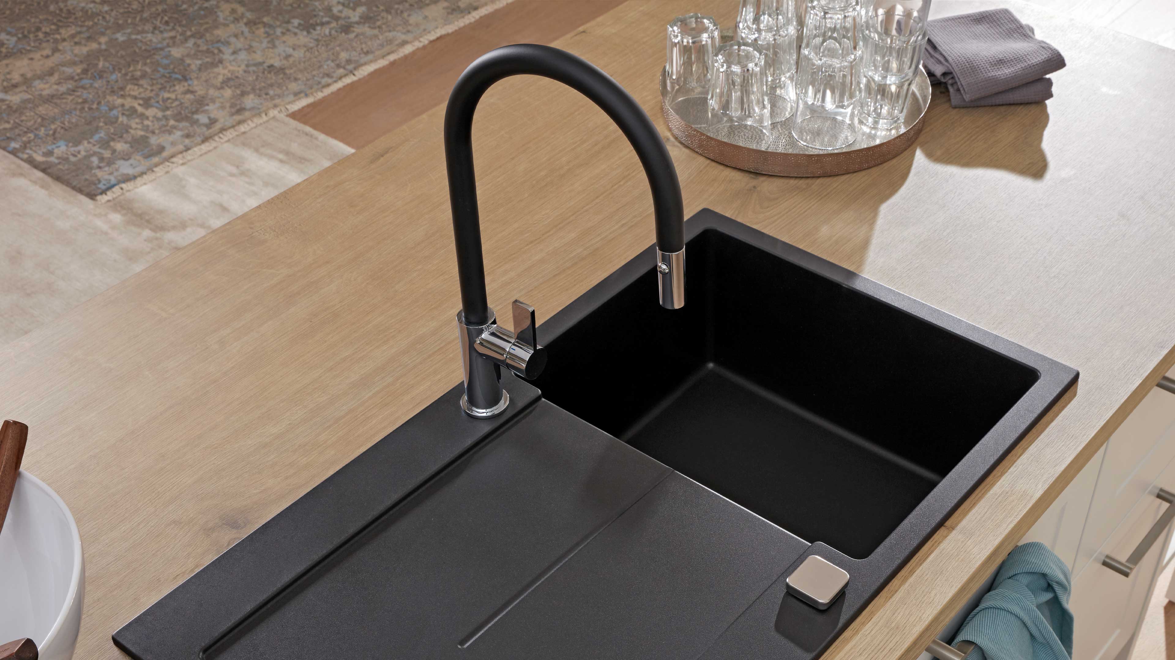 Schwarzes, matt wirkendes Einbauspülbecken mit rechteckiger Einzelwanne, integrierter Abtropffläche und hoher schwarz-chrom Armatur.