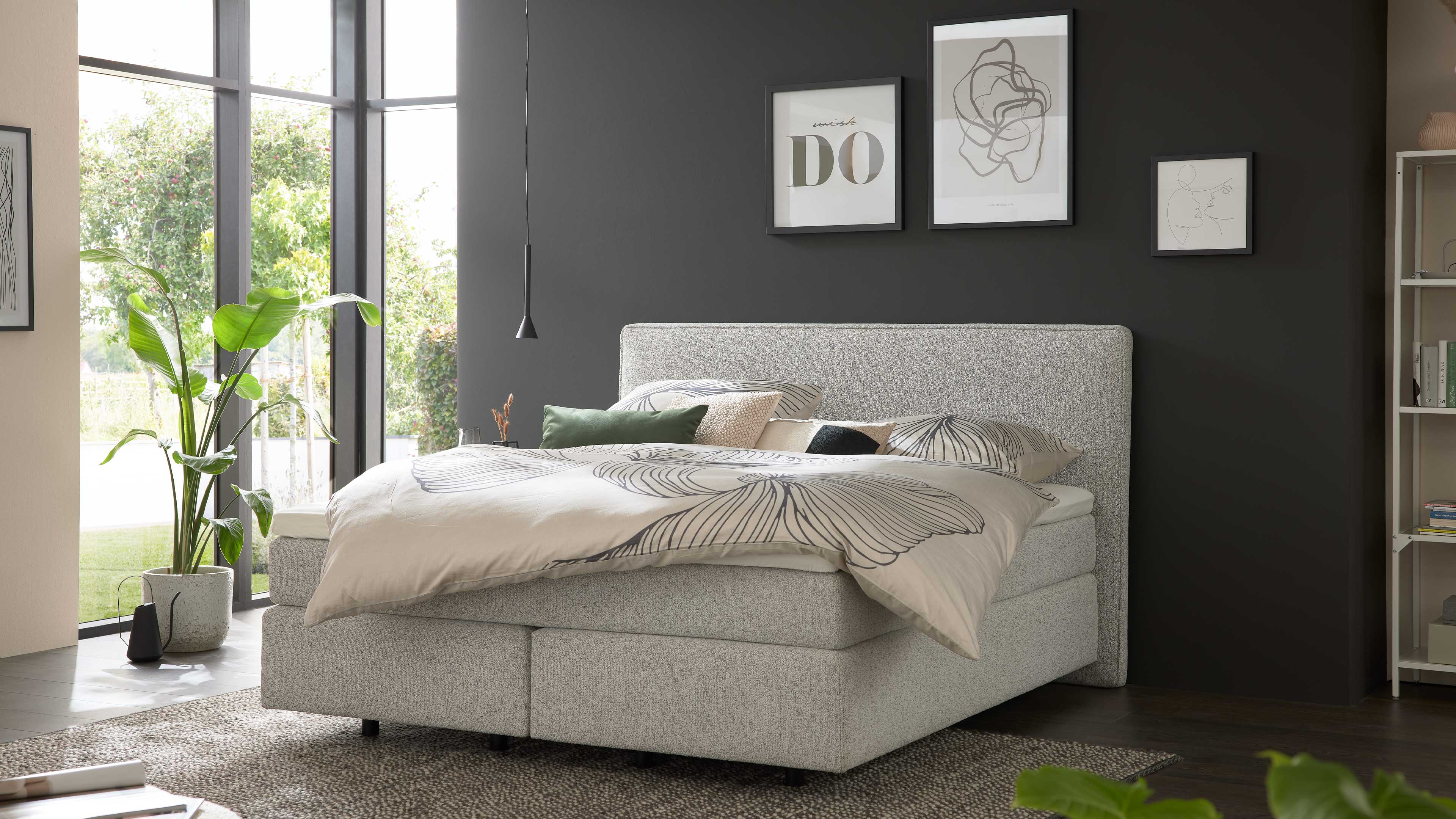 Boxspringbett mit gepolstertem Kopfteil, hellgrauem Stoffbezug und hoher Matratze für gleichmäßigen Liegekomfort