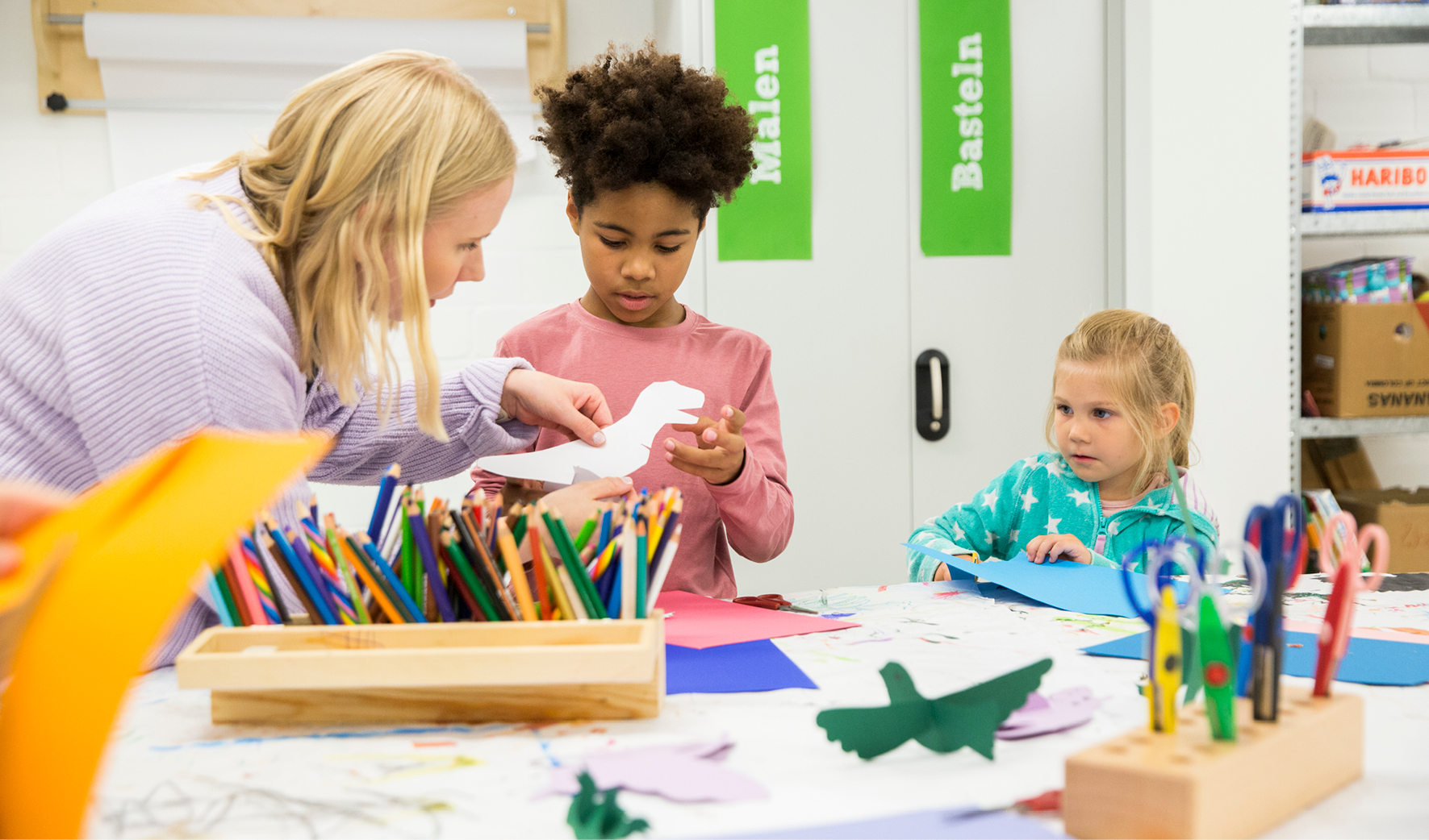 Kinder basteln zusammen mit einer Mitrarbeitering von SOS-Kinderdorf