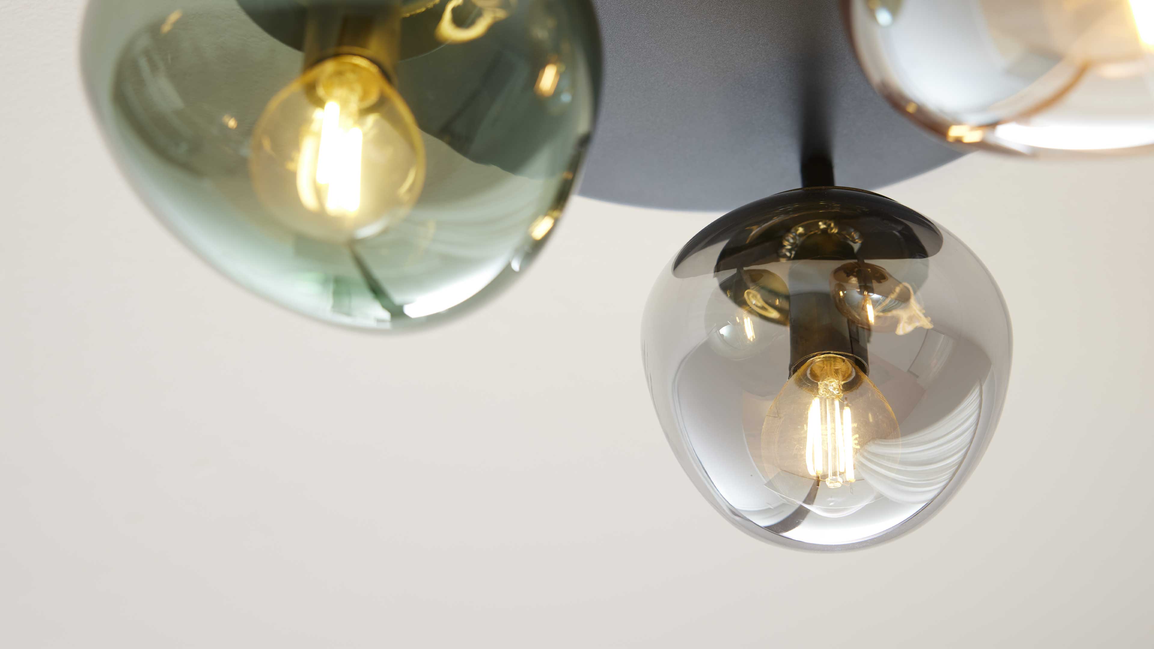 Drei hängende Glaslampen mit unterschiedlich getönten, runden Schirmen (grün, rauchgrau) und sichtbaren Filamentbirnen.