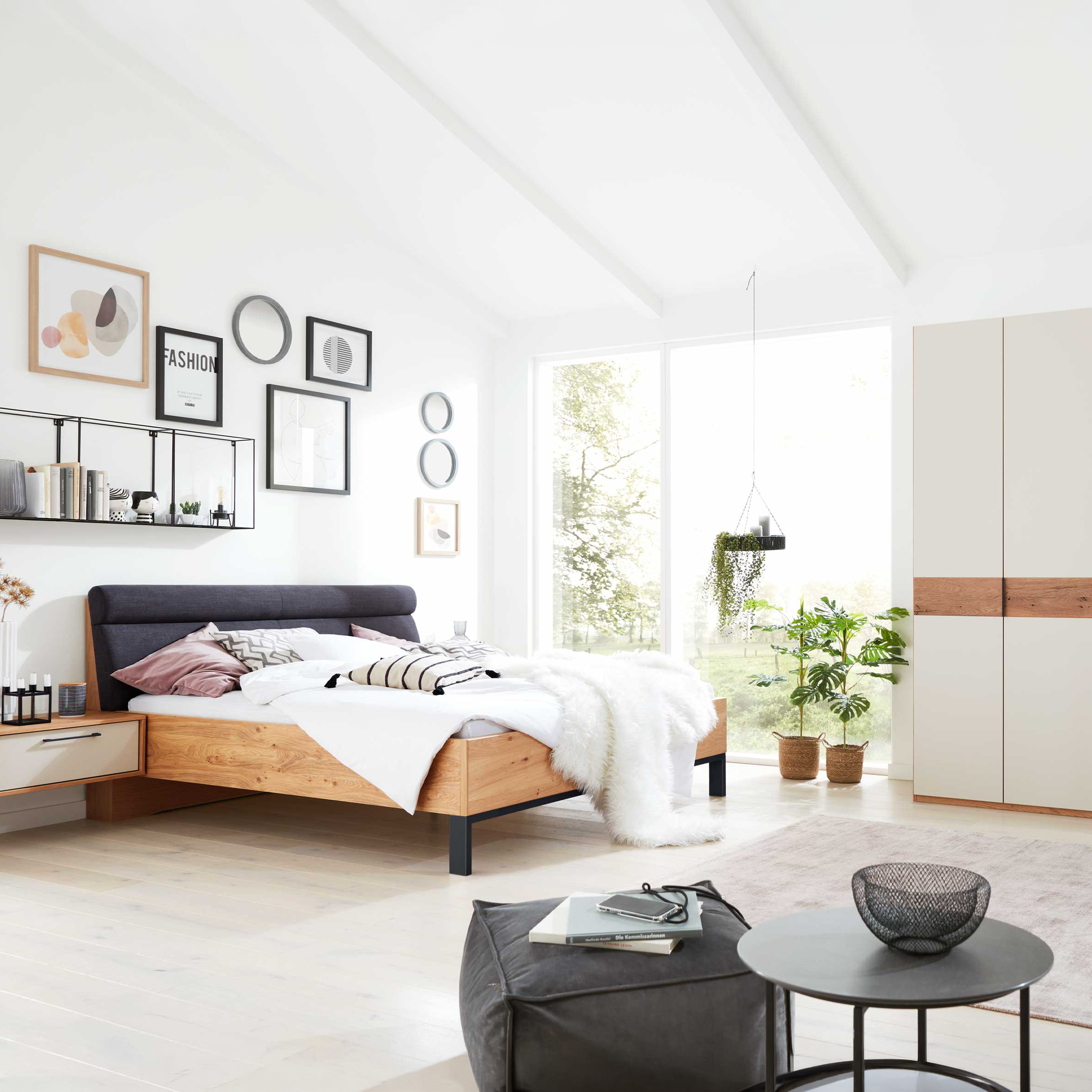 Bett mit dunkelgrauem Kopfteil, Holzrahmen und schwebendem Nachttisch links, großer heller Kleiderschrank mit Holzstreifen rechts.