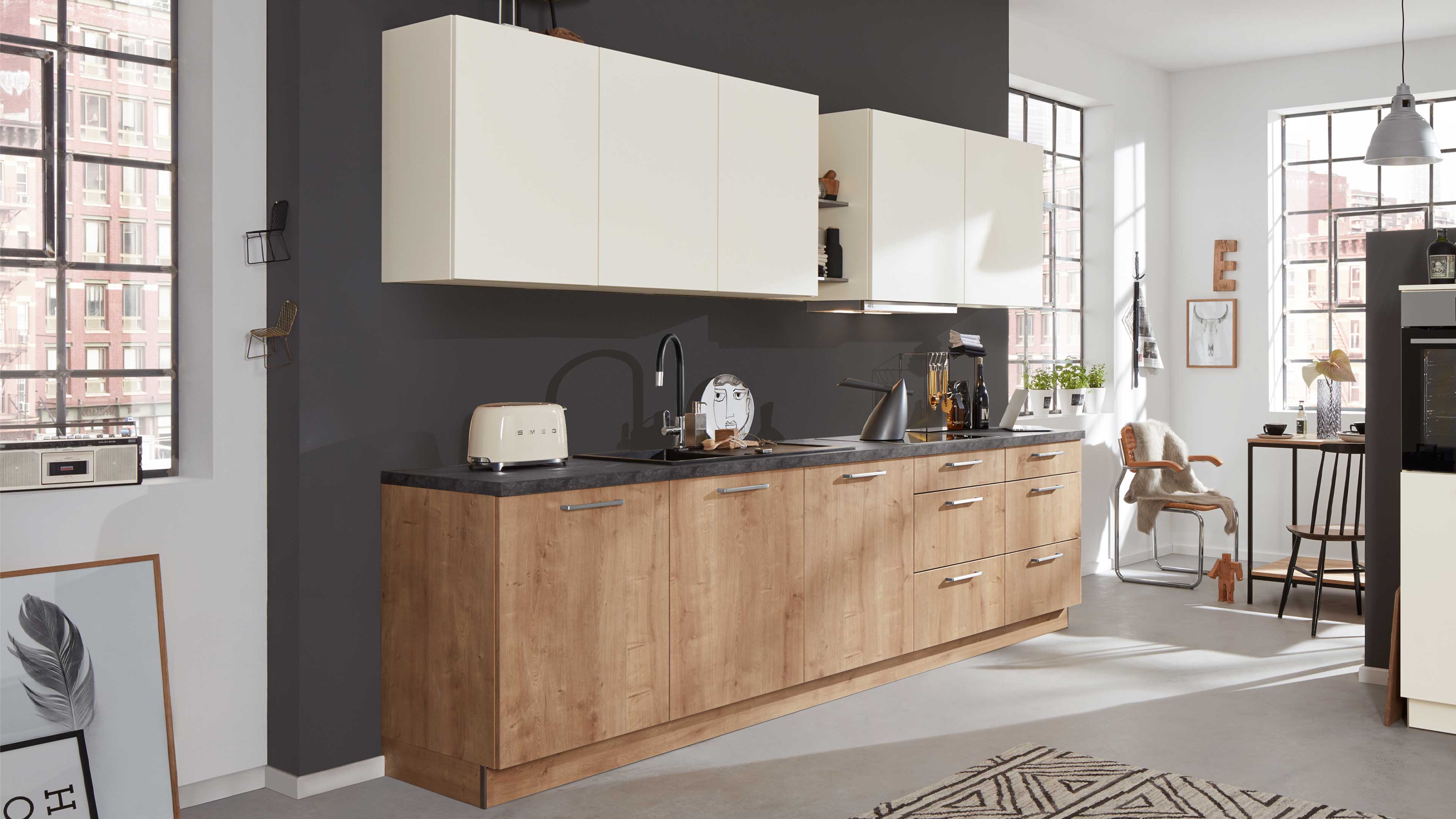 Lange Küchenzeile mit holzfarbigen Unterschränken, dunkelgrauer Arbeitsplatte und cremefarbenen Hängeschränken.