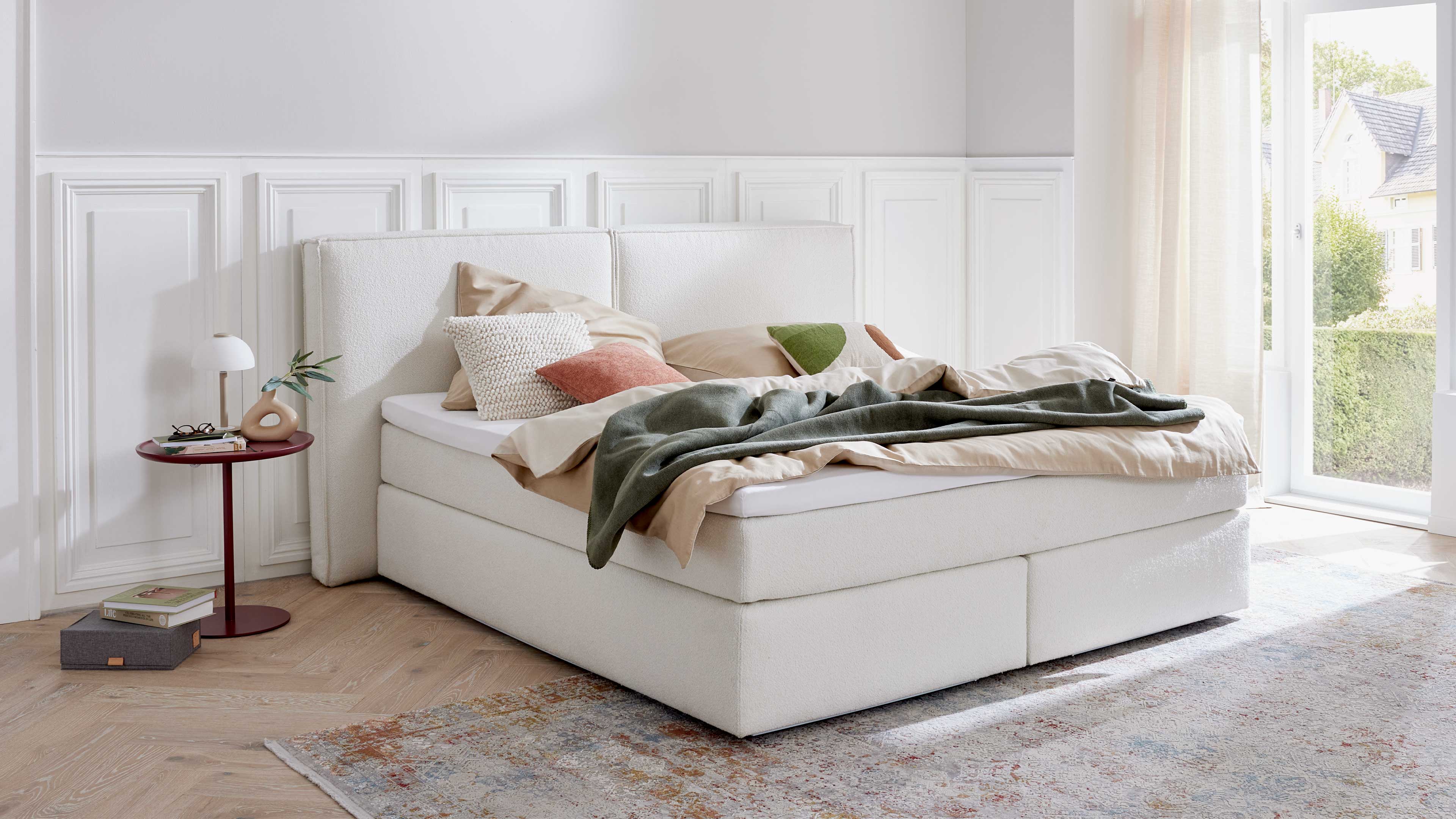 Boxspringbett mit gepolstertem Kopfteil, weißem Stoffbezug und hoher Matratze für komfortables Liegen