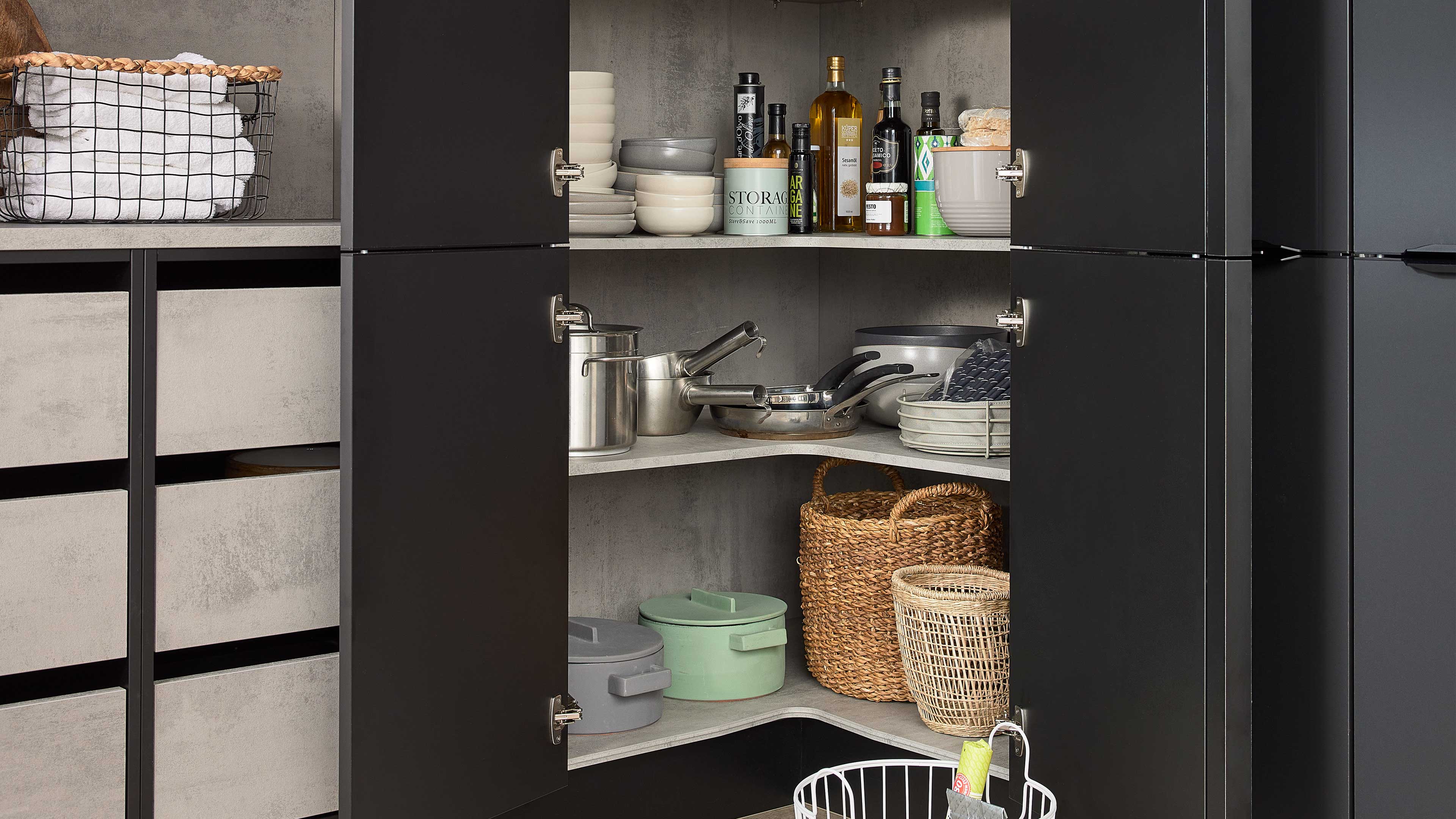 Offener schwarzer Eckschrank mit regalförmigen Ablagen, gefüllt mit Töpfen, Pfannen, Schalen, Vorratsdosen und geflochtenen Körben.