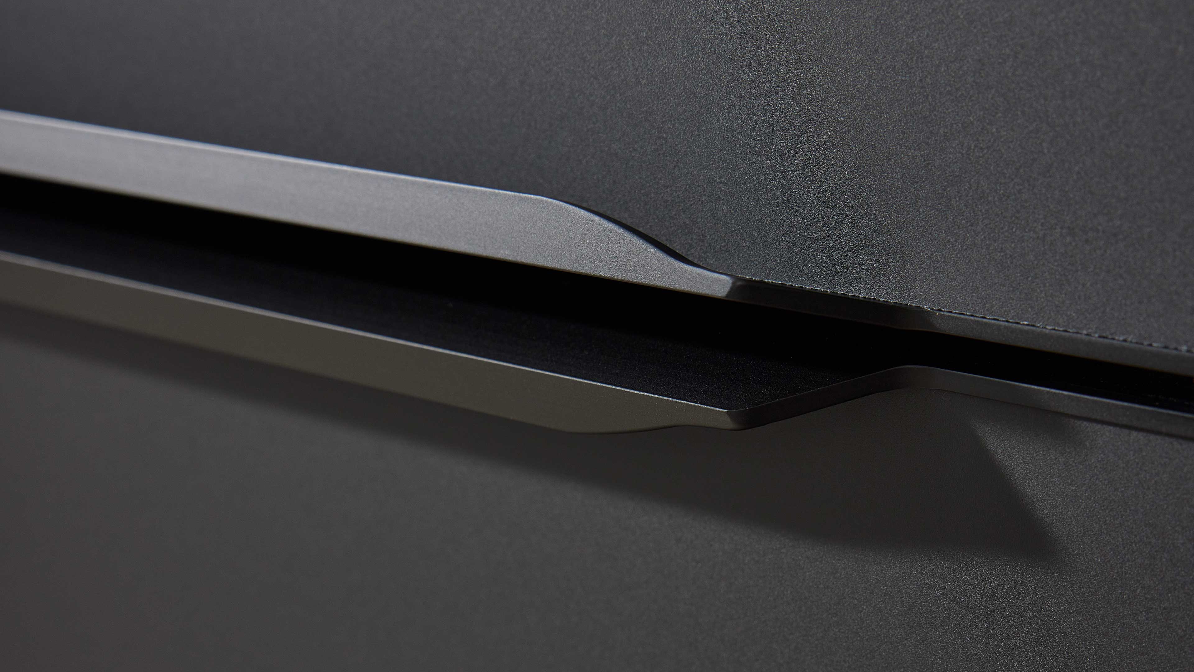 Nahaufnahme zweier dunkler, flacher Schubladen- oder Türgriffe mit schmalem Spalt auf mattschwarzer, leicht strukturierter Oberfläche.