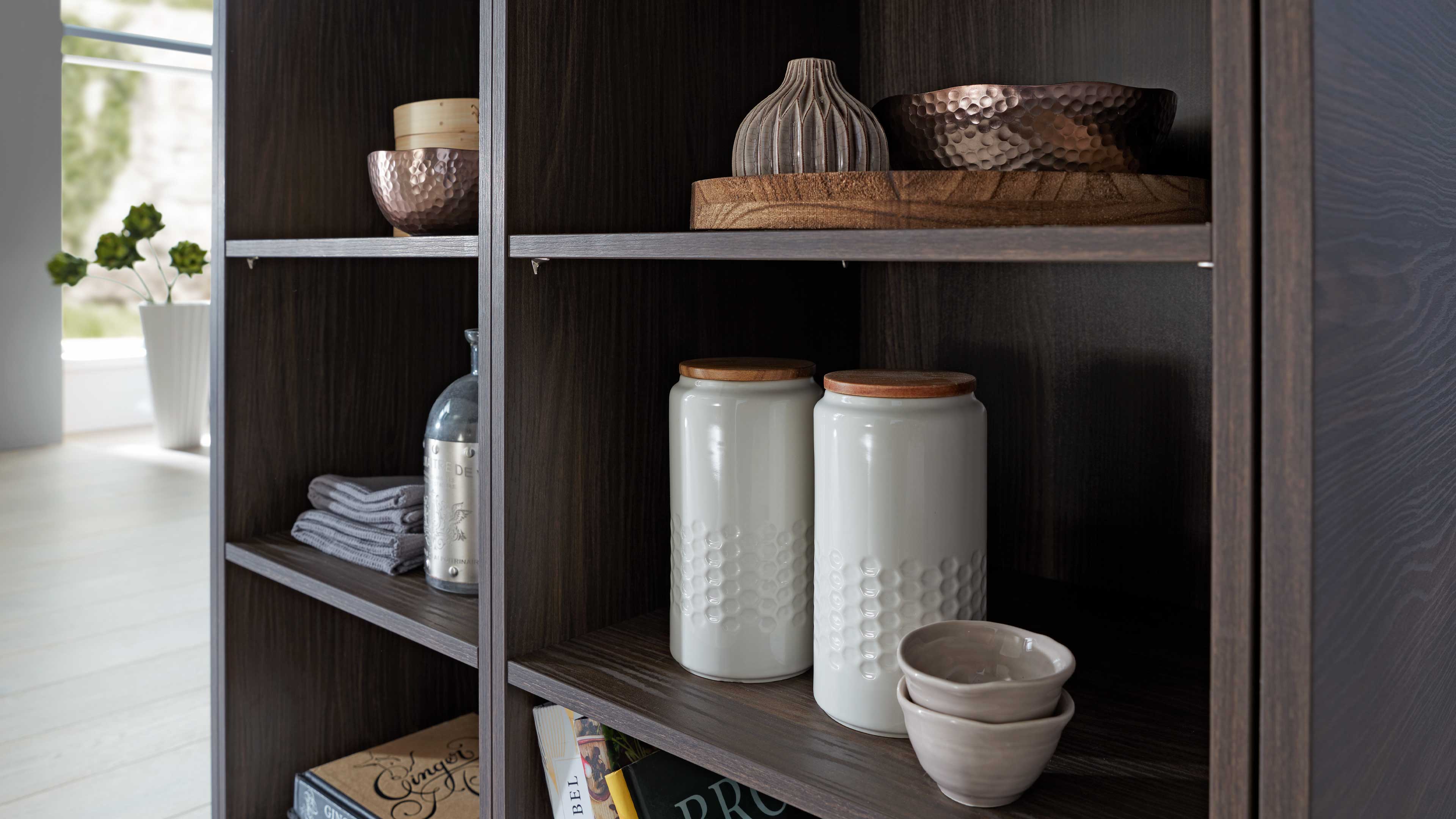 Offenes Regal aus dunklem Holz mit quadratischen Fächern, darin zwei weiße Keramikdosen mit Holzdeckeln und zwei kleine Schalen.