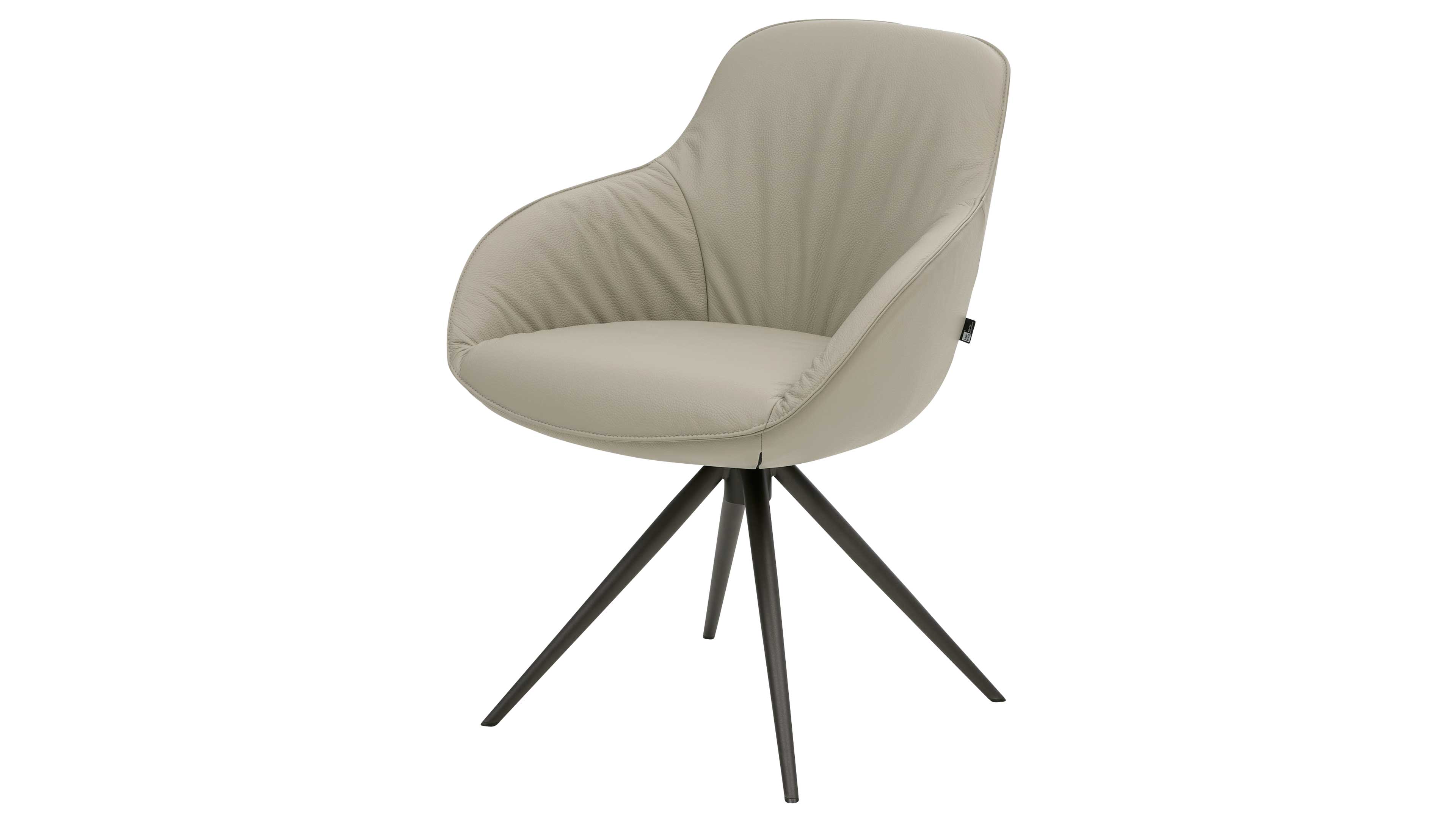 Gepolsterter hellbeiger Schalensessel mit integrierten Armlehnen, sichtbarer Seitenlasche und dunklem, vierarmigem Metallsternfuß.