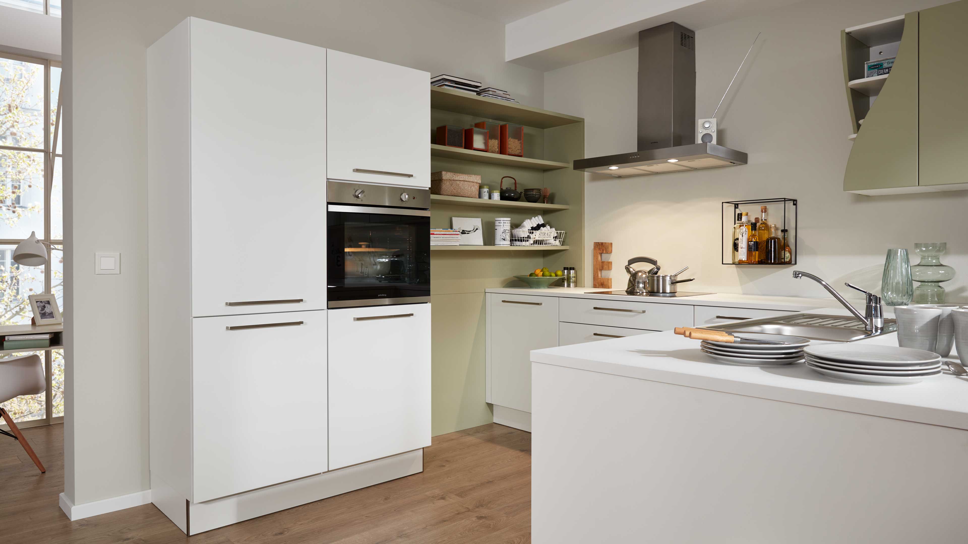 Moderne Einbauküche mit weißen Fronten, eingebautem Ofen, offenem hellgrünem Regal, Edelstahl-Dunstabzug und Insel.