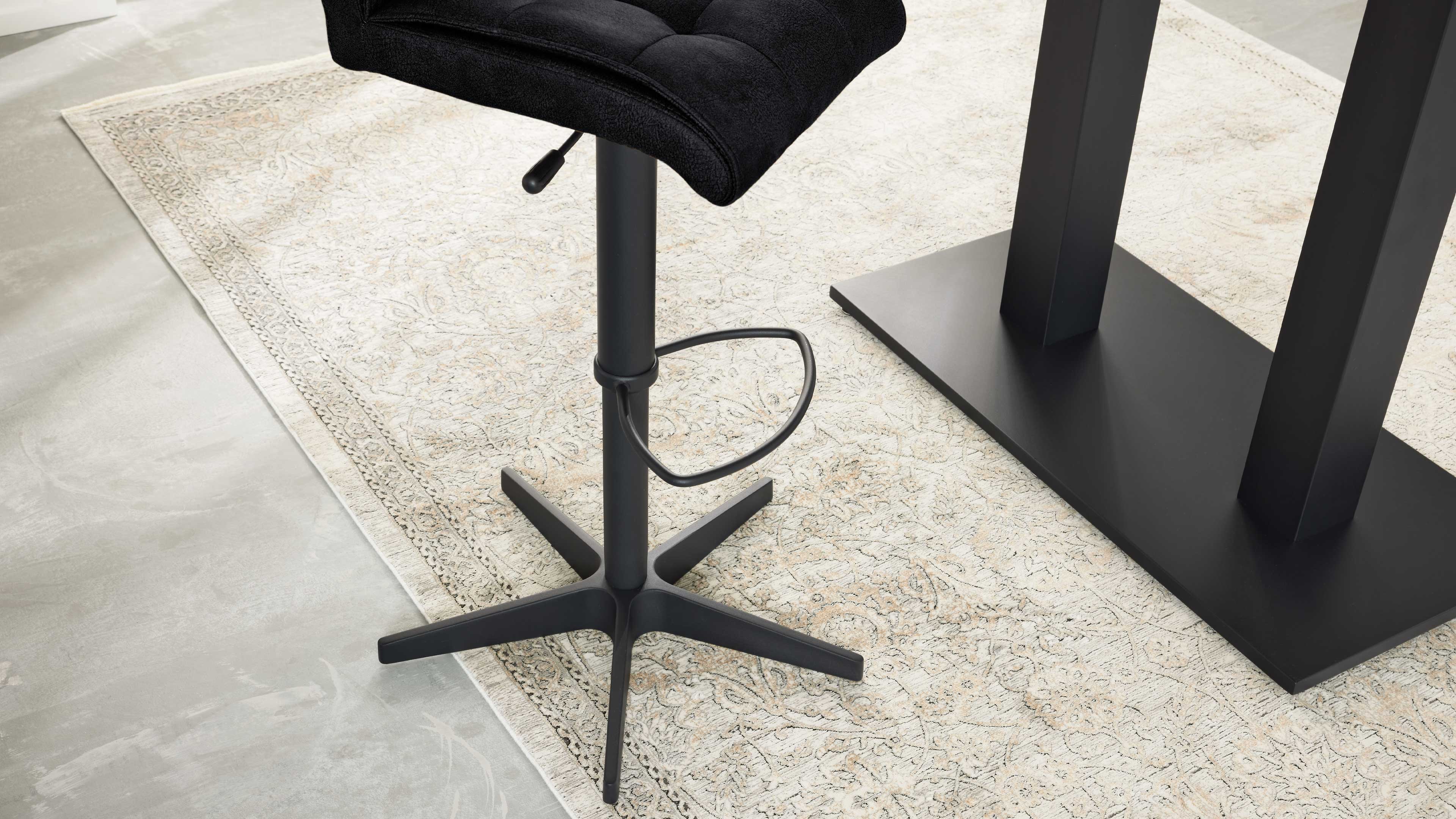Schwarzer Barhocker mit gepolstertem Sitz, Säule, Fußring und Fünf-Stern-Basis neben schwarzer Tischsäule auf hellem Ornamentteppich.