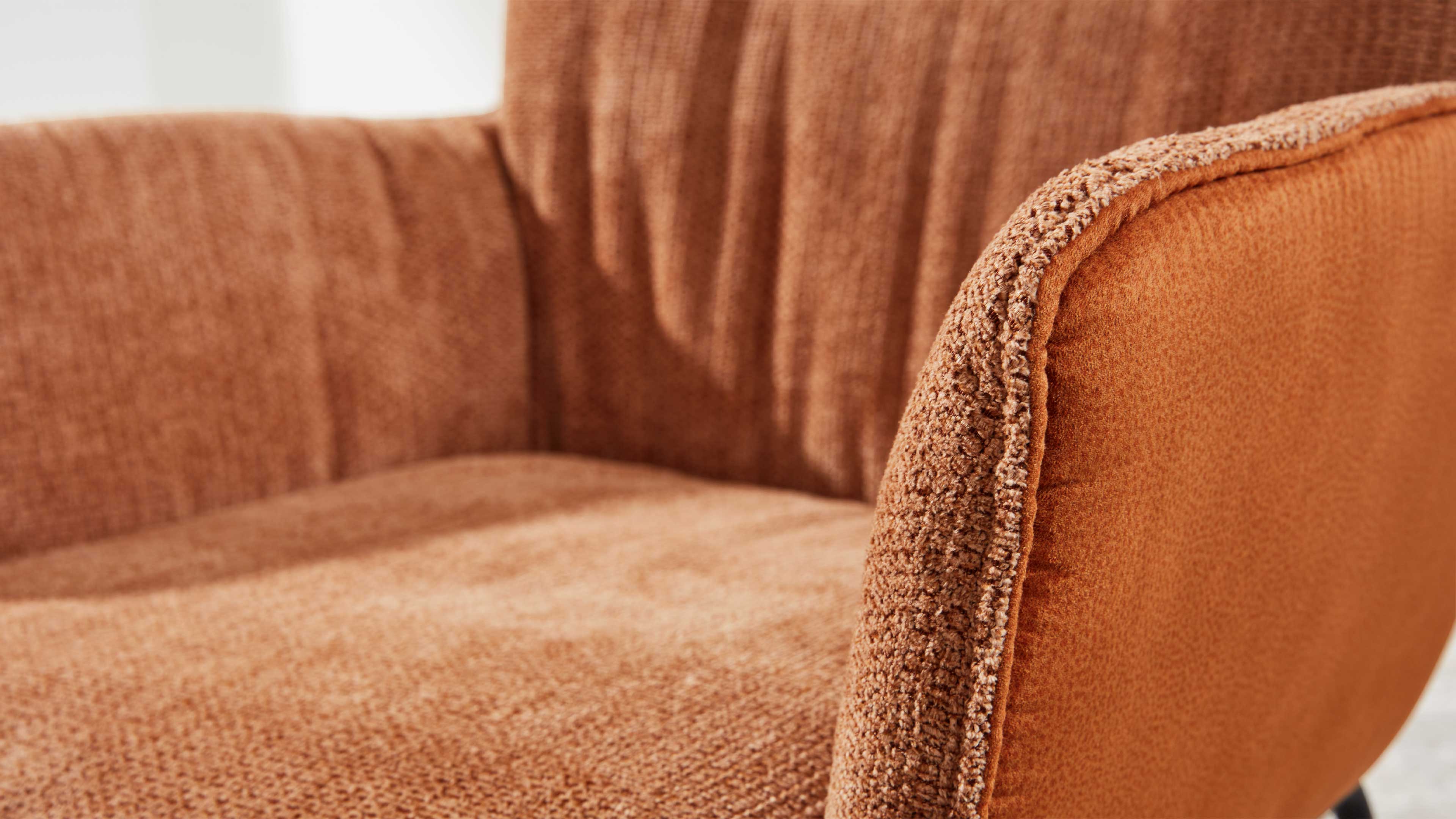 Terrakottafarbener, stoffbezogener Sessel mit strukturierter Sitzfläche, Rückenlehne und gepolsterter Armlehne mit sichtbarer Kedernaht.